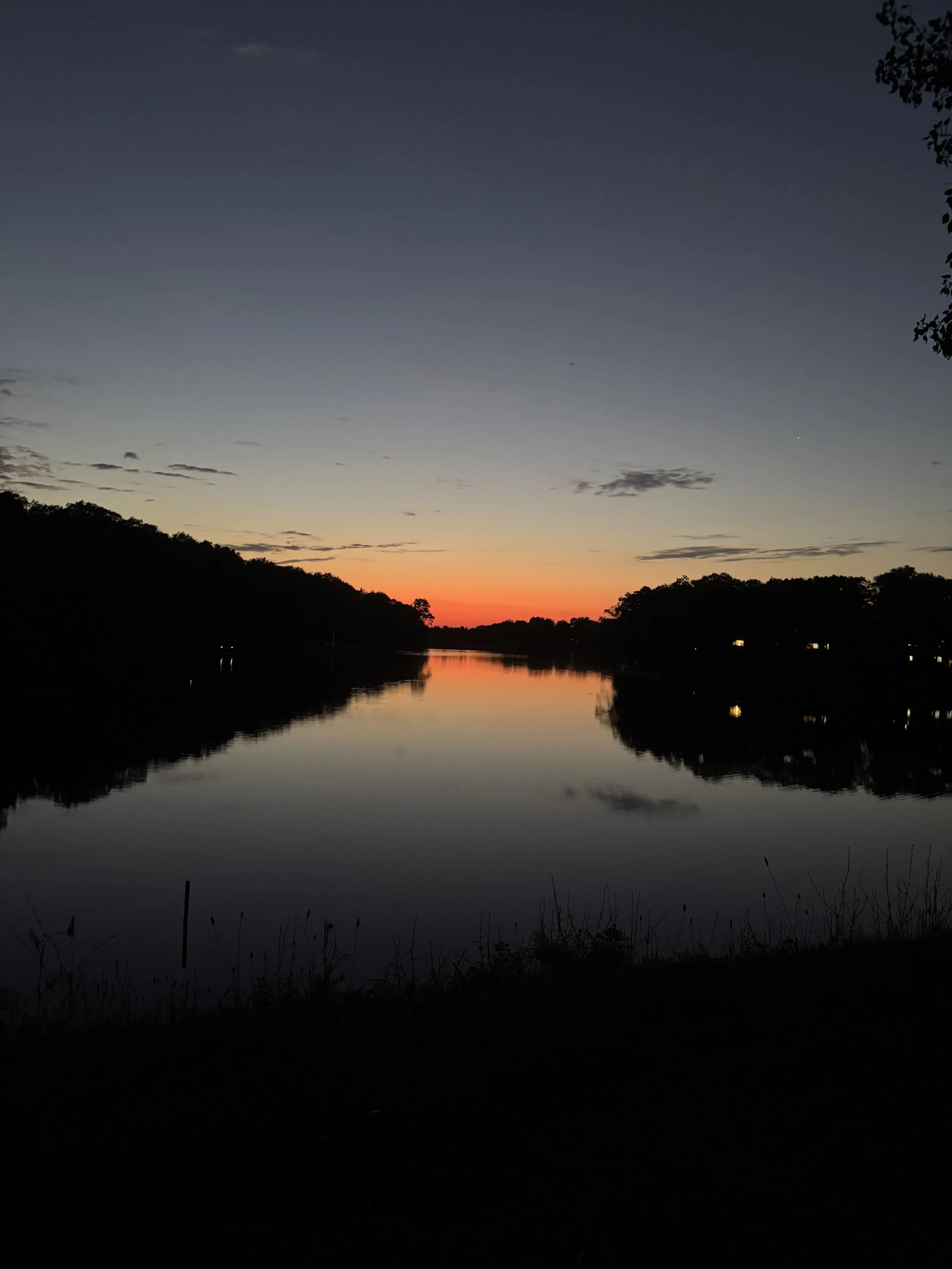 Sunset over a calm river, with silhouetted trees on both sides and a reflection of the sky in the water.