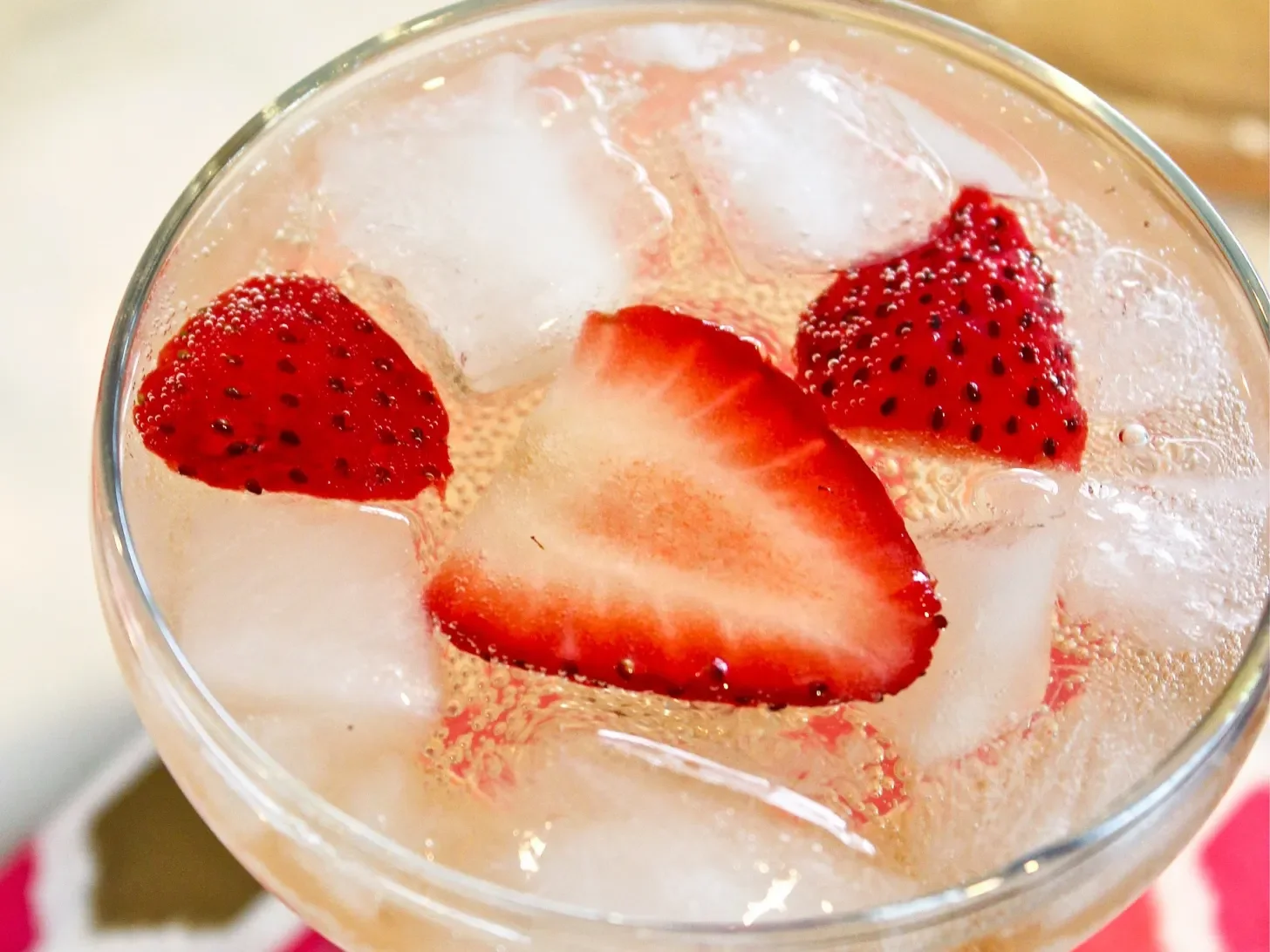 A glass of pink drink with ice cubes and sliced strawberries.