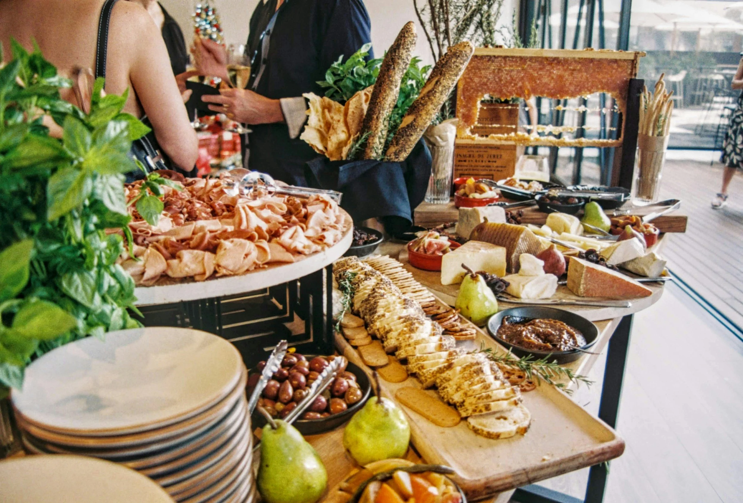 A buffet table with assorted cheeses, breads, fruits, olives, and charcuterie at a social gathering.
