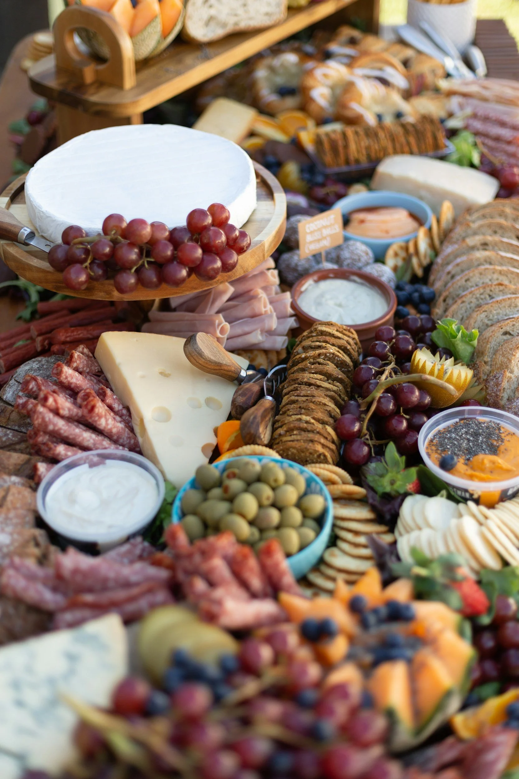 Assorted cheeses, grapes, cookies, crackers, olives, meats, and dips on a table for a cheese board or platter.