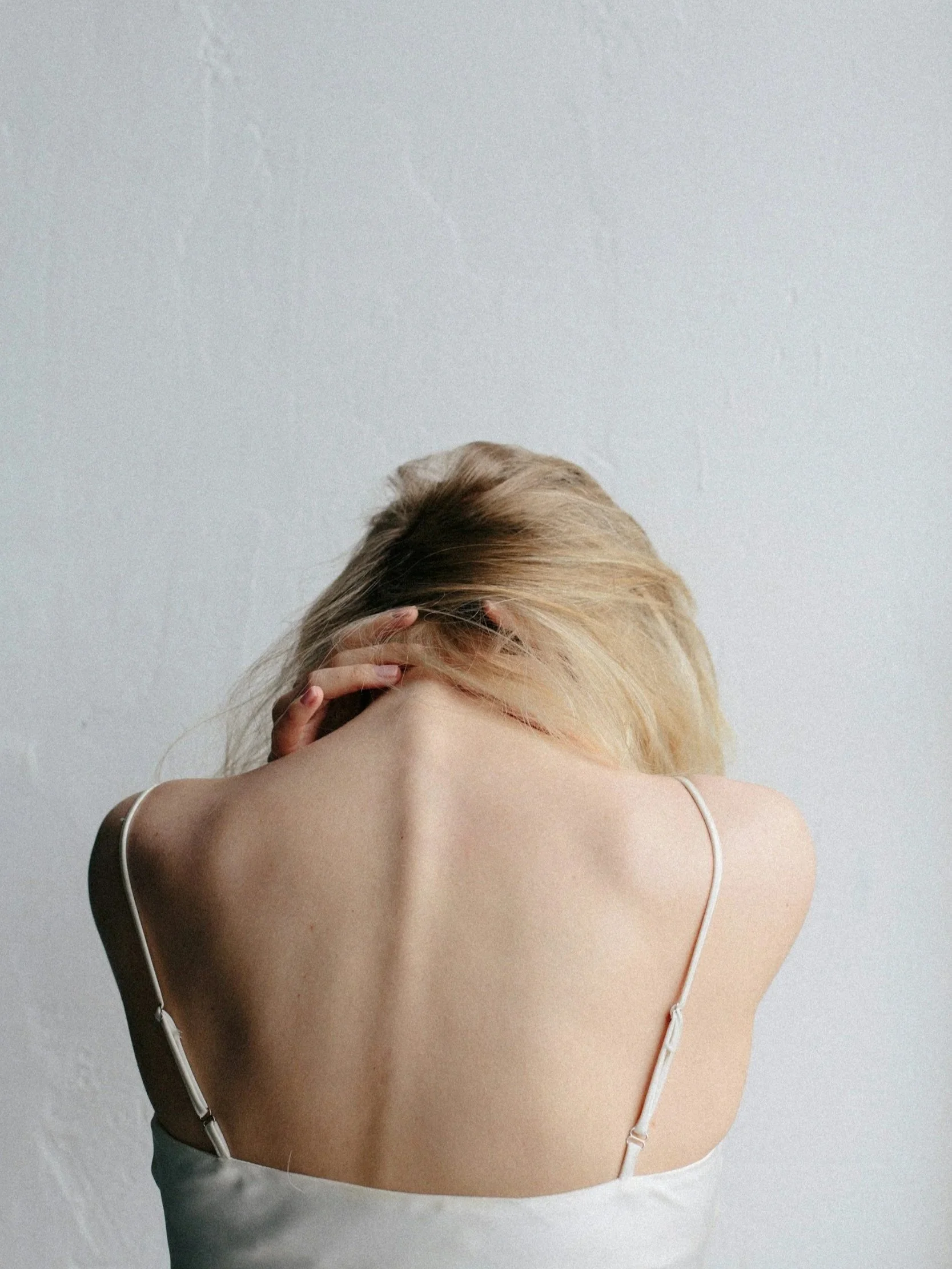 Close-up van een vrouw met blond haar, zij houdt haar hoofd vast met één hand, tegen een witte muur achtergrond.
