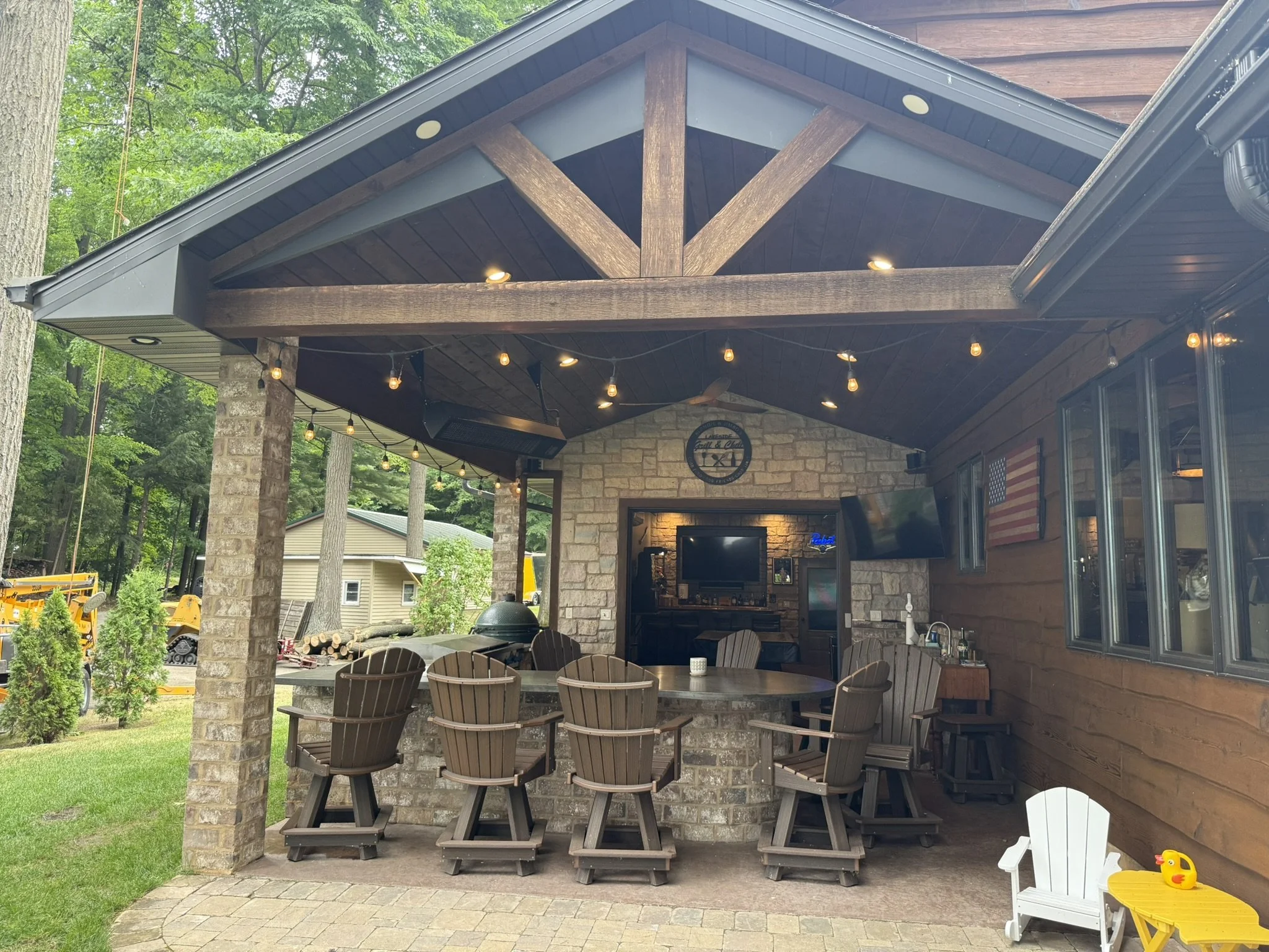 Full build modern/rustic outdoor kitchen, with timberwork, brick bar/peninsula, stained concrete counters, built in big green egg, steel cooktop, char broiler and burners, built-in stainless-steel cabinets, stone clad accent wall, stamped concrete fl