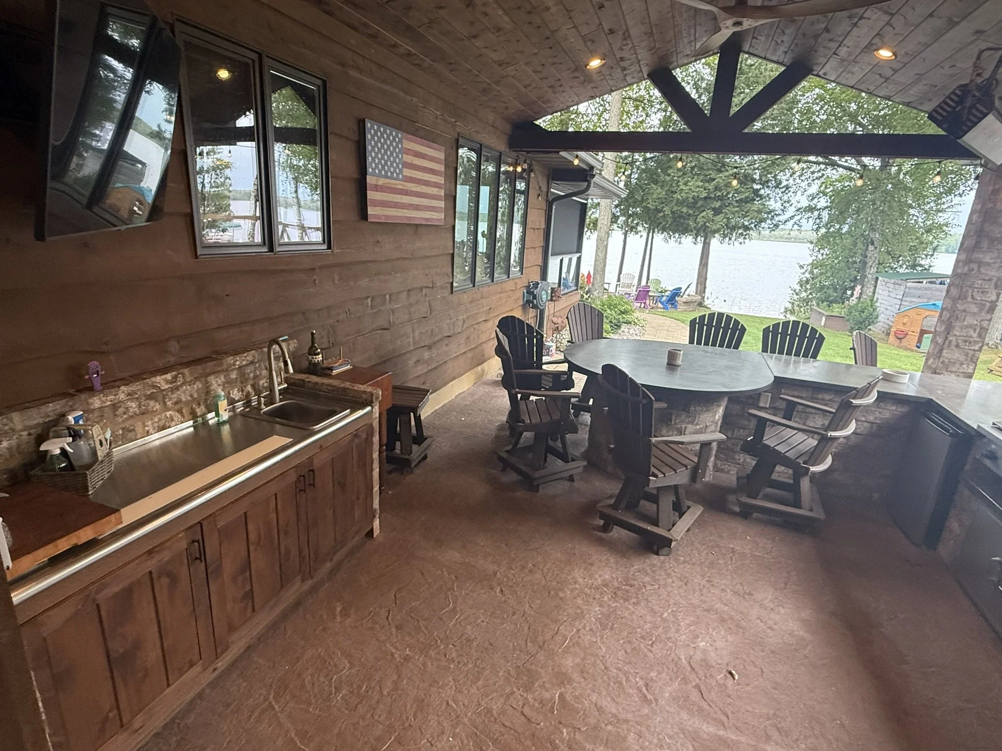 Full build modern/rustic outdoor kitchen, with timberwork, brick bar/peninsula, stained concrete counters, built in big green egg, steel cooktop, char broiler and burners, built-in stainless-steel cabinets, stone clad accent wall, stamped concrete fl