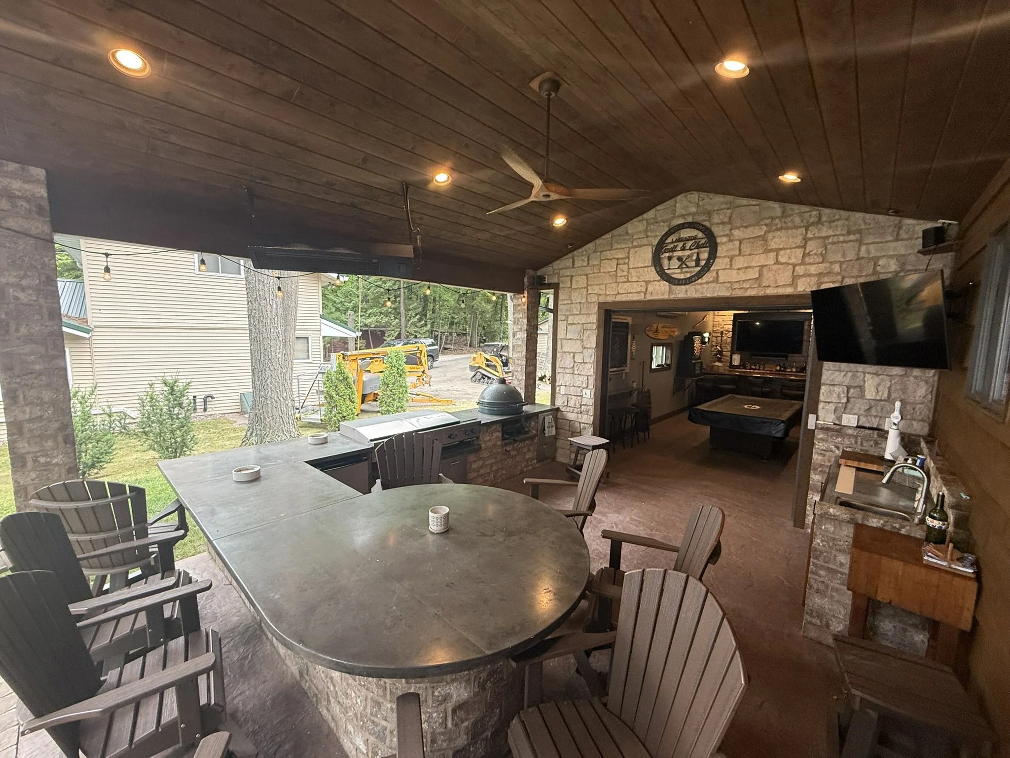 Full build modern/rustic outdoor kitchen, with timberwork, brick bar/peninsula, stained concrete counters, built in big green egg, steel cooktop, char broiler and burners, built-in stainless-steel cabinets, stone clad accent wall, stamped concrete fl