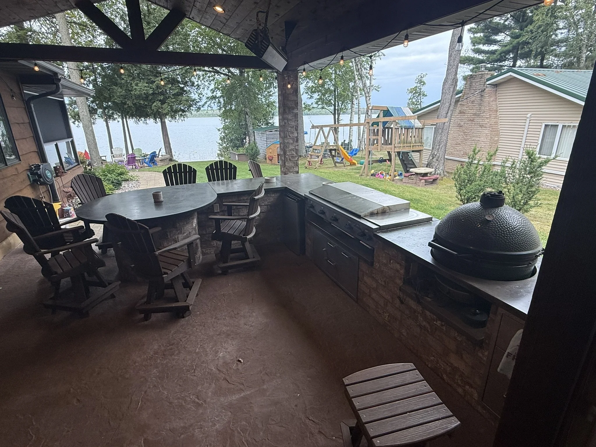 Full build modern/rustic outdoor kitchen, with timberwork, brick bar/peninsula, stained concrete counters, built in big green egg, steel cooktop, char broiler and burners, built-in stainless-steel cabinets, stone clad accent wall, stamped concrete fl