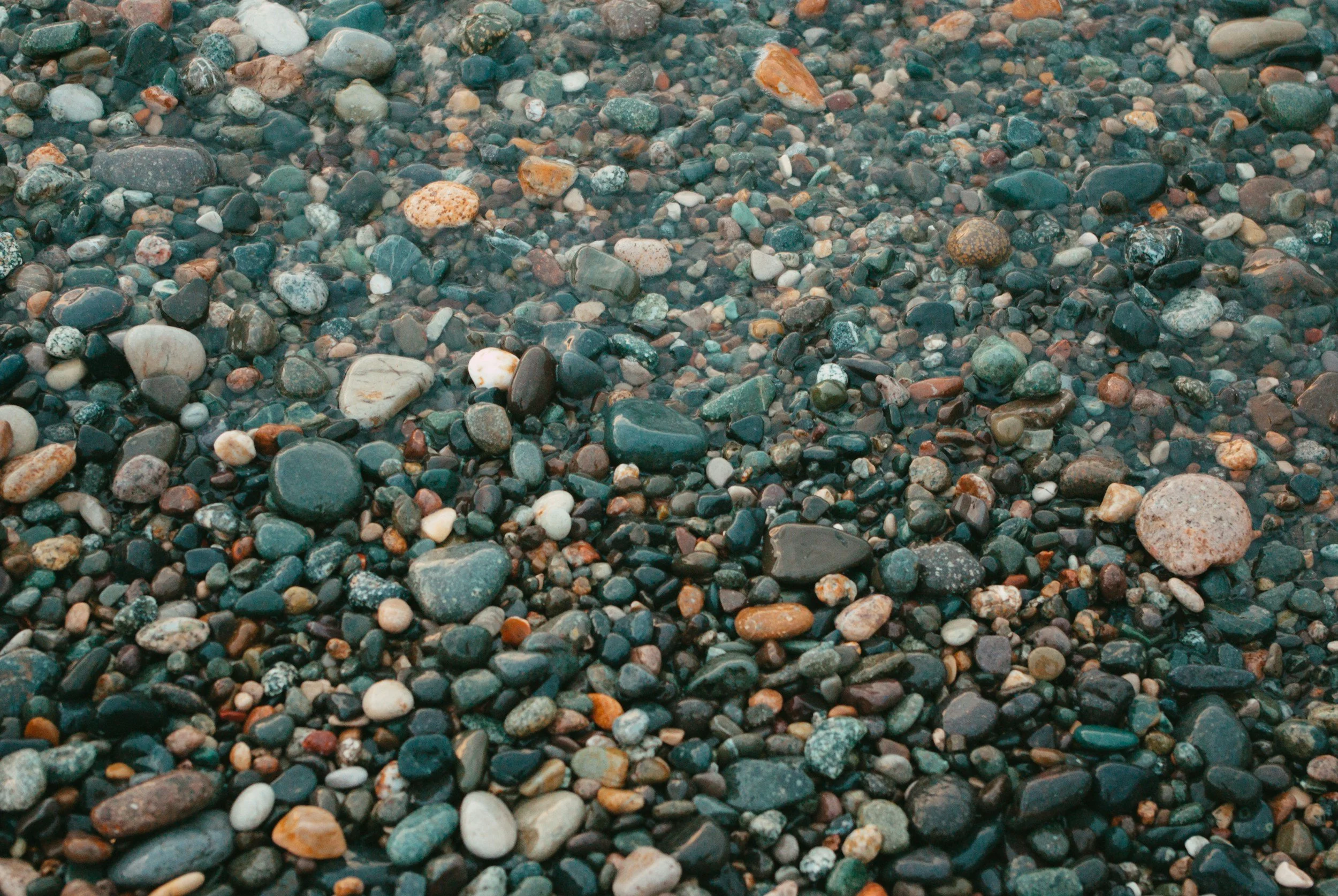 Close-up view of a beach surface covered with multicolored small and medium-sized pebbles and stones.