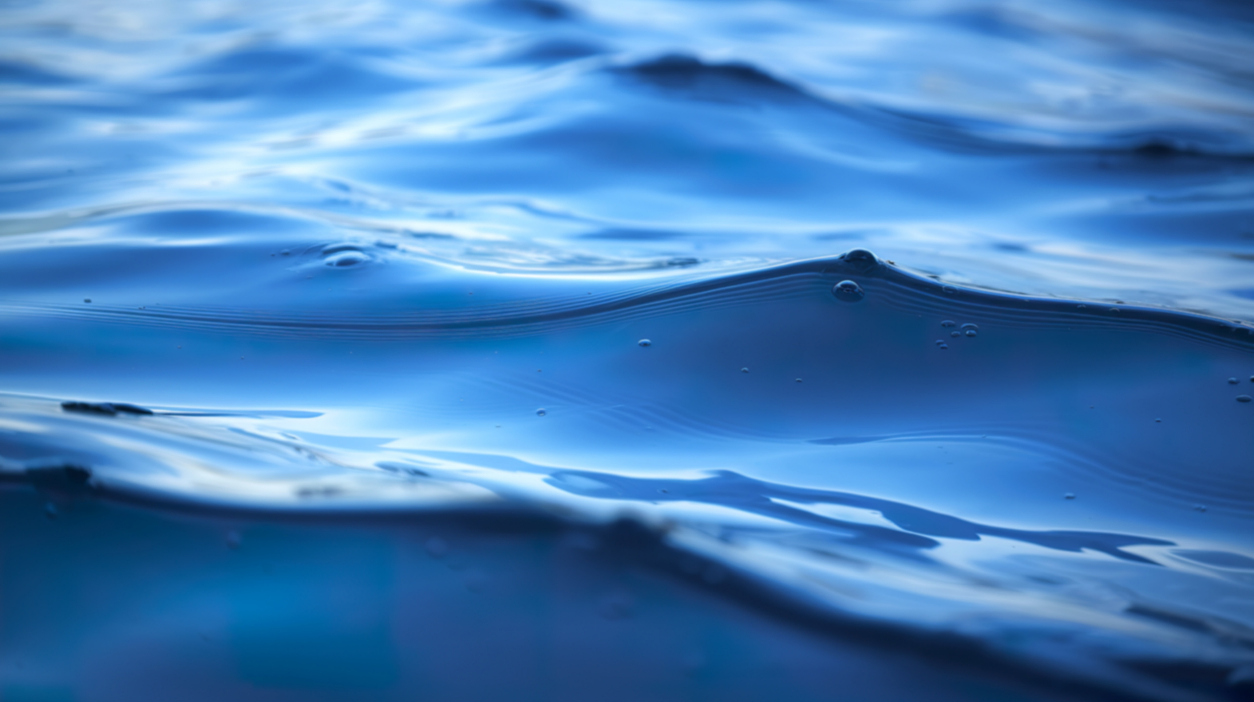 Close-up of blue ocean water with gentle waves and small bubbles.