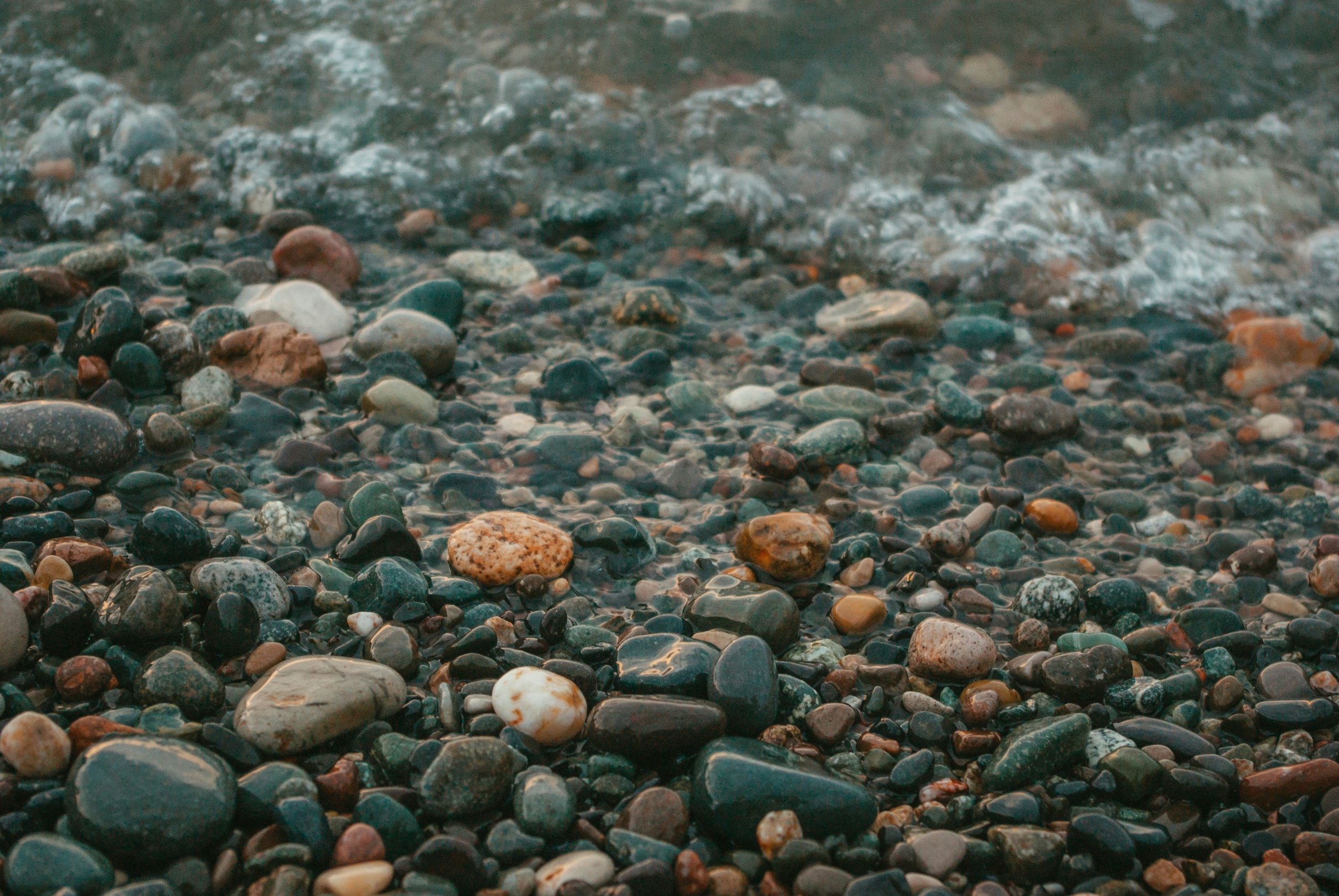 Close-up of a pebble beach with small, smooth stones and some water waves in the background.