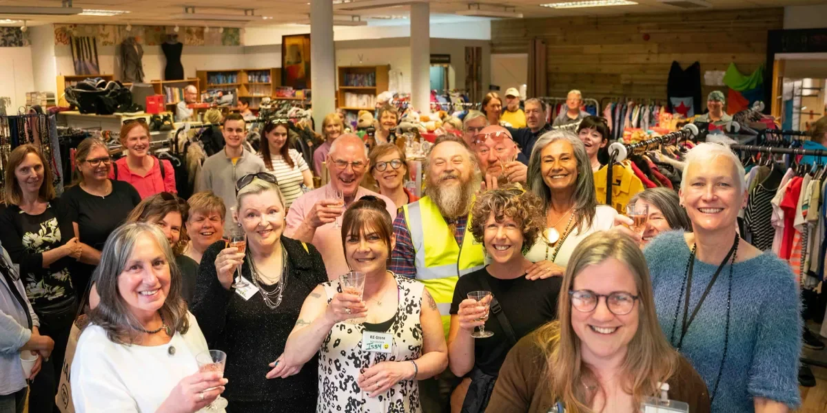 Group of smiling people inside a thrift store, holding glasses and celebrating.