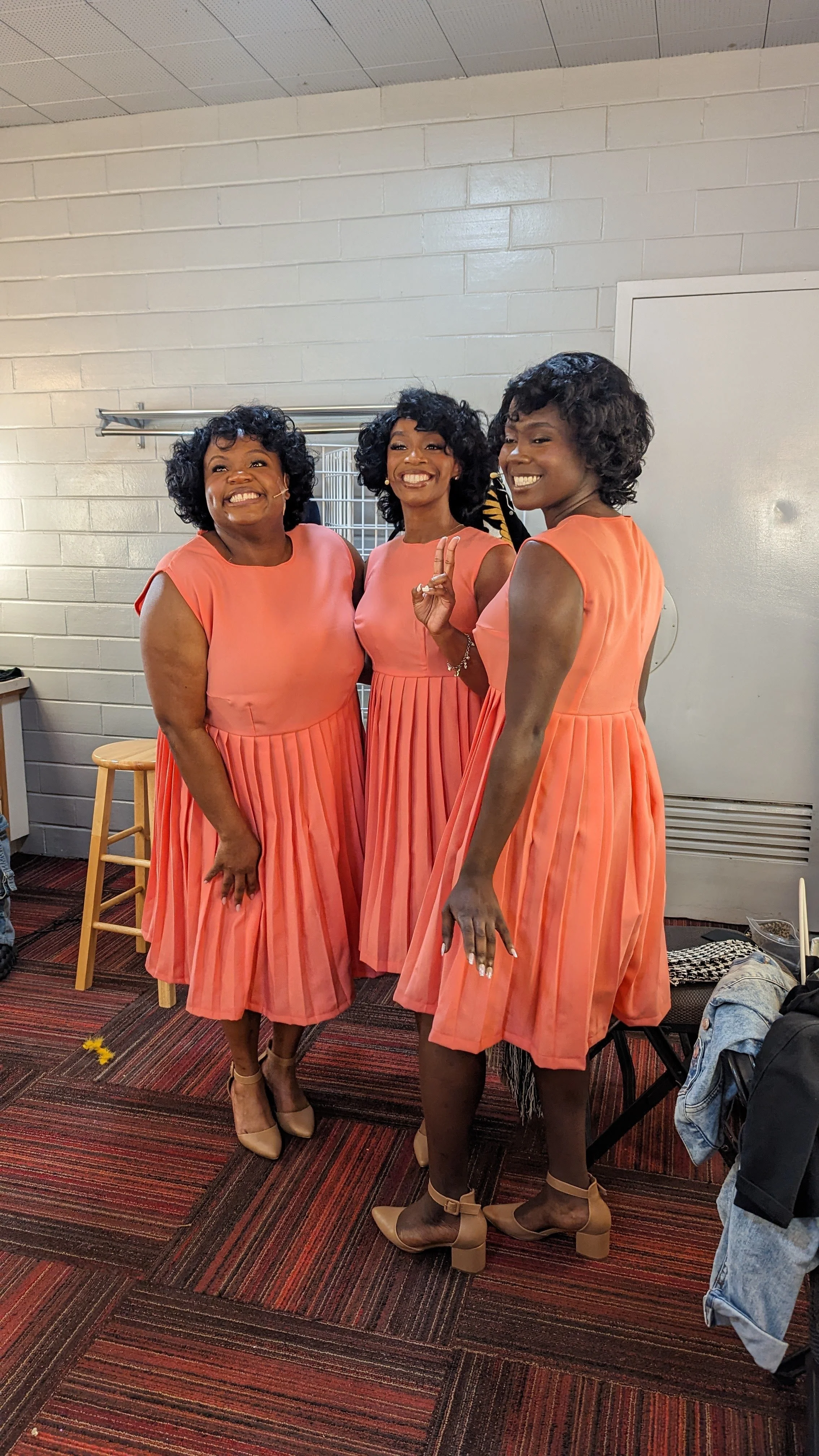 Three women in peach, pleated, sleeveless dresses smiling