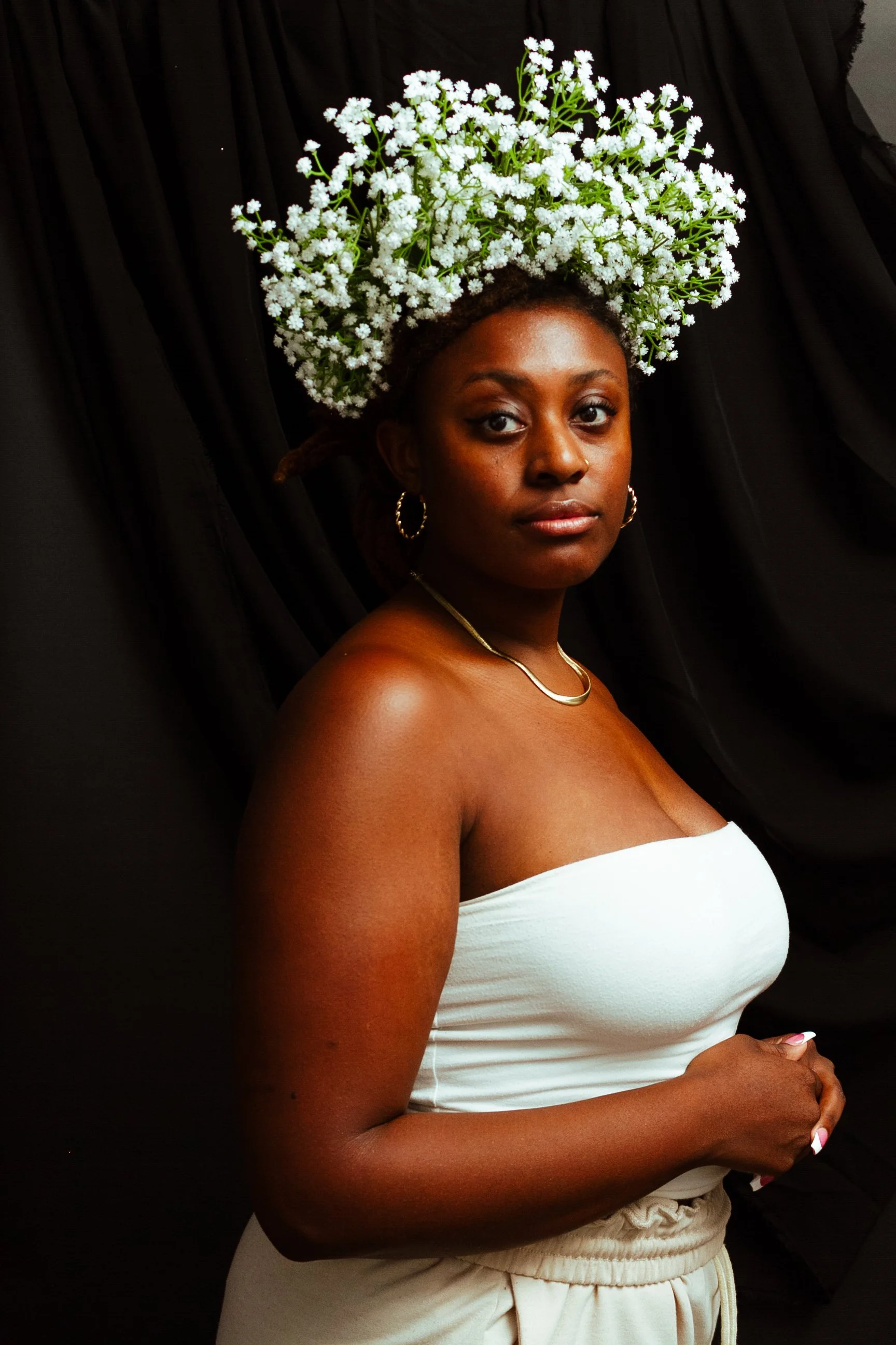 woman wearing a white, strapless top and a white floral bridal crown against a black fabric backdrop