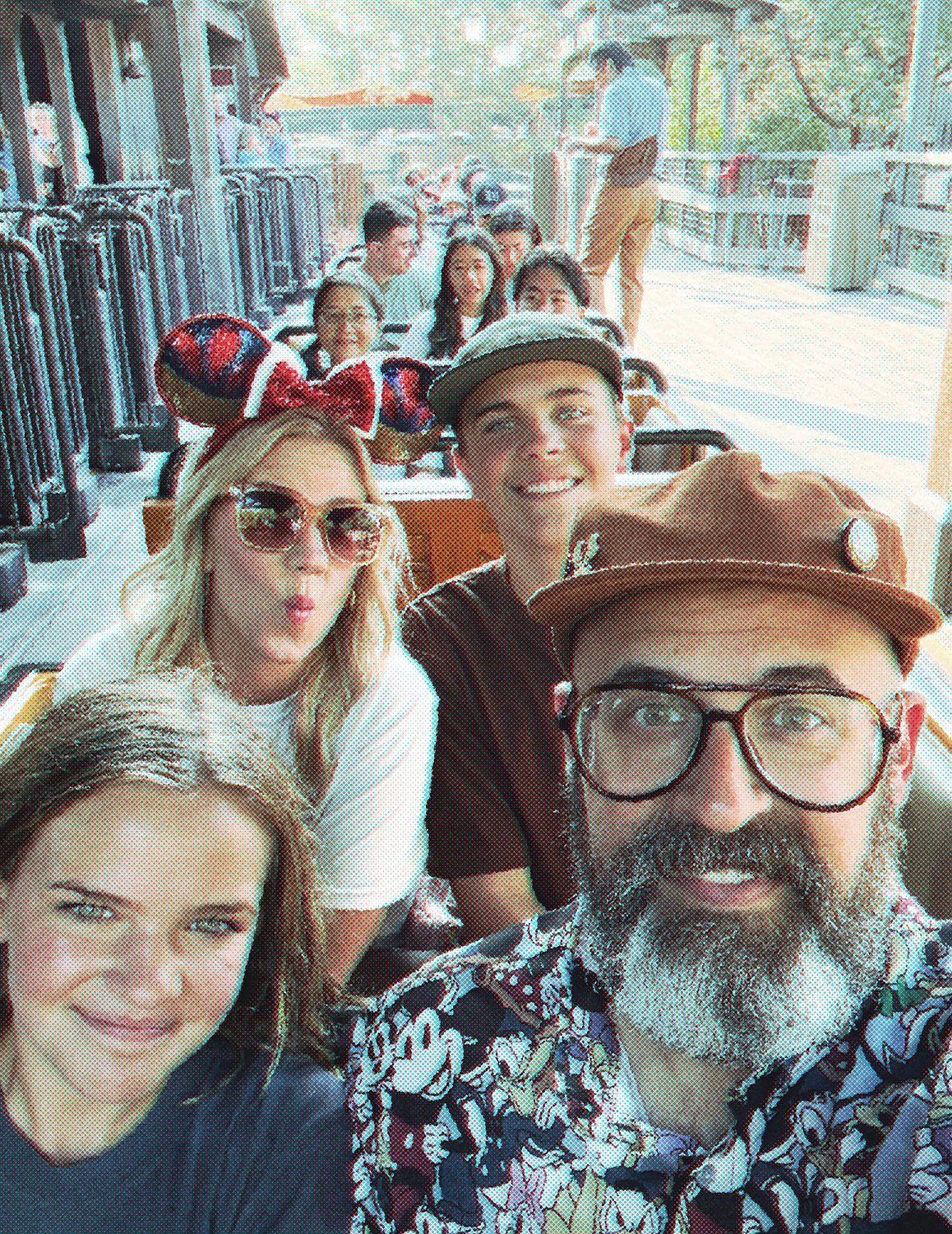 Group of diverse friends sitting on a roller coaster ride, smiling and taking a selfie, with amusement park background.