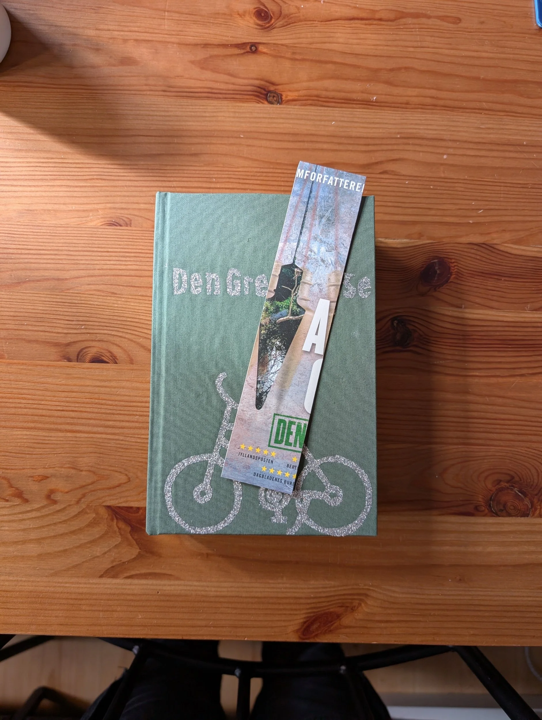 A book with a bicycle illustration on the cover and a bookmark placed on it, resting on a wooden surface.