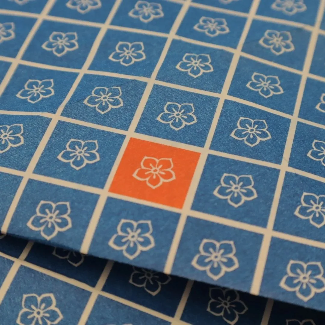 Close-up of a blue pamphlet with white floral patterns, featuring one red square with a white floral pattern.