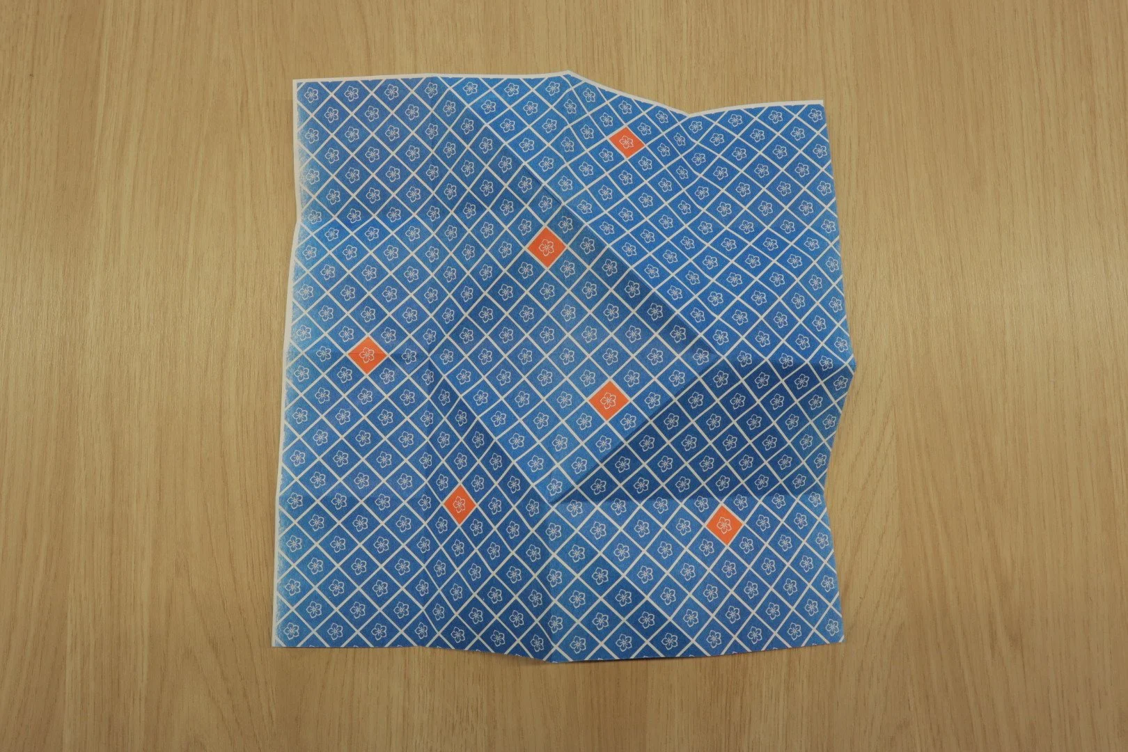 A divided blue and white patterned sheet of paper with orange diamonds on a light wooden surface.