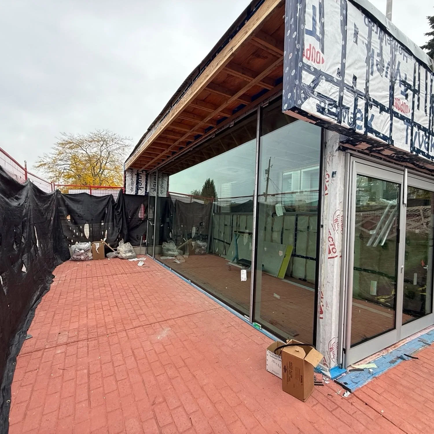 Full-height exterior glass walls beside a brick patio on a building undergoing renovation.