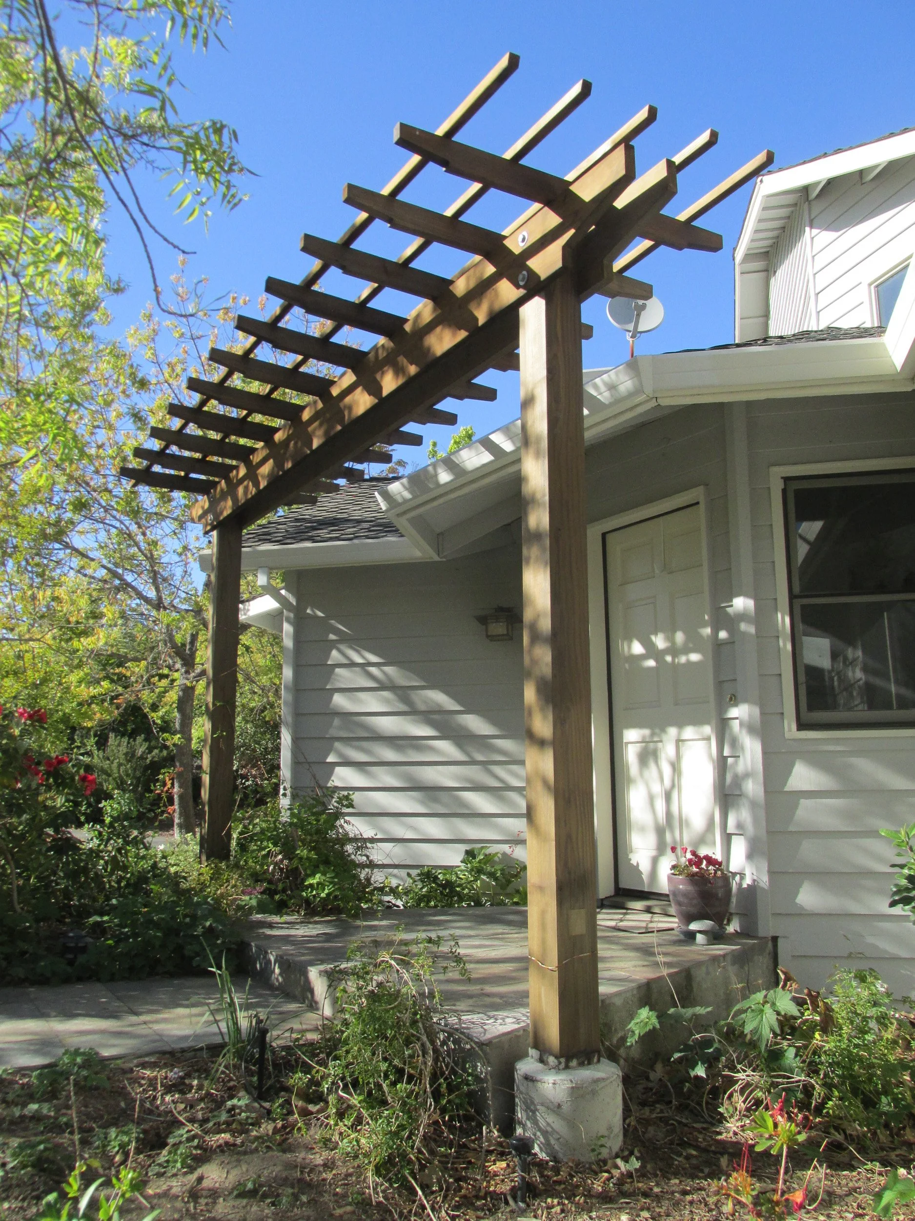 An overhead wood pergola structure japanese style around a residential garden front entry