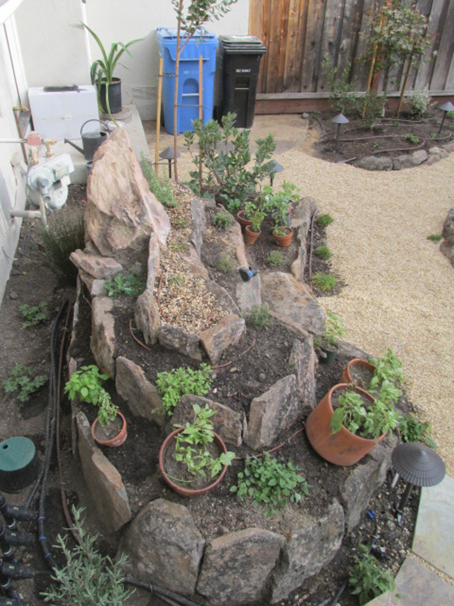 Stones and boulders form a raised spiral herb garden in a residential landscape.
