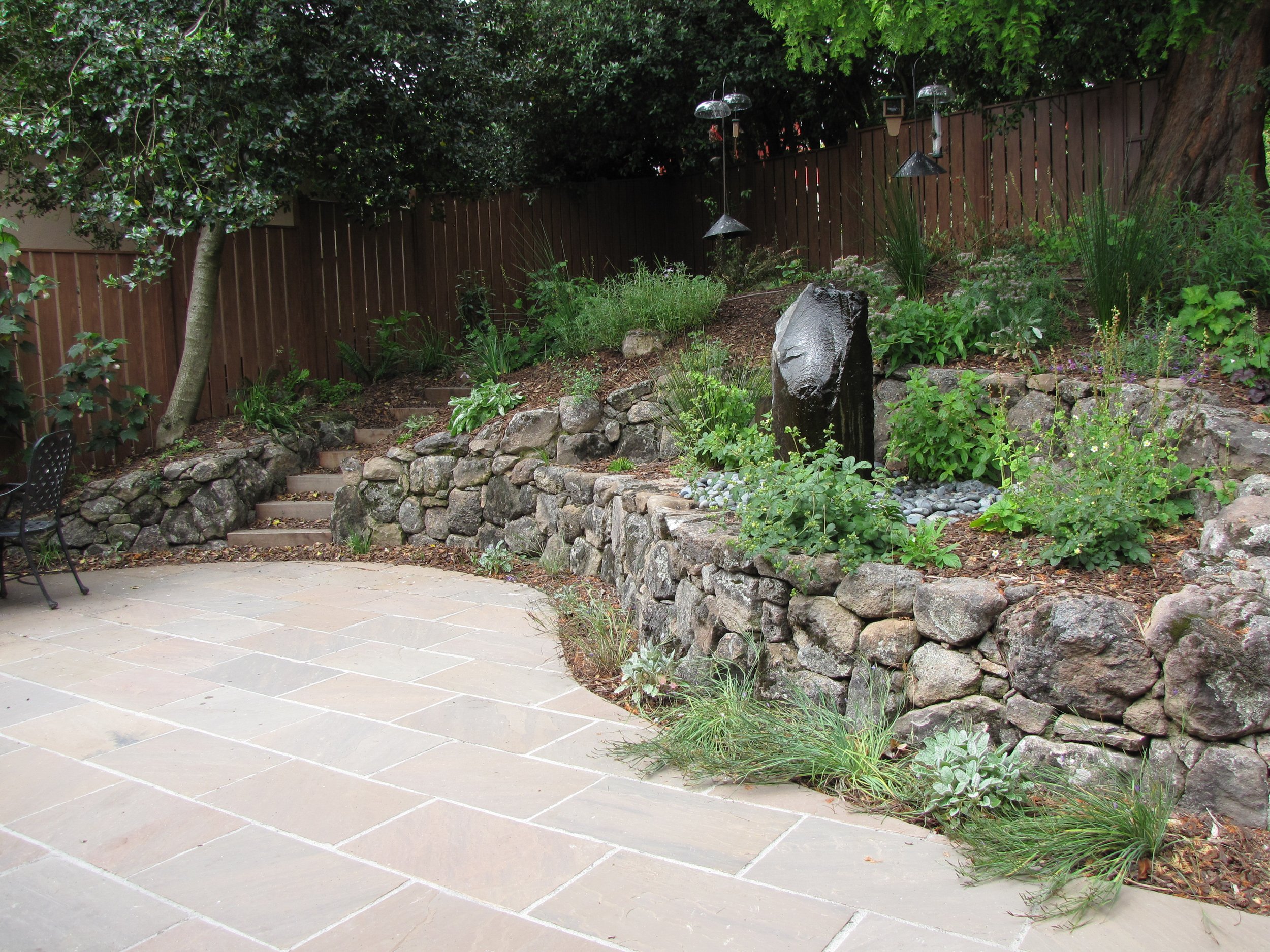 Front garden in Berkeley hills with stone patio moss rock retaining walls fountain and california native plants bird friendly