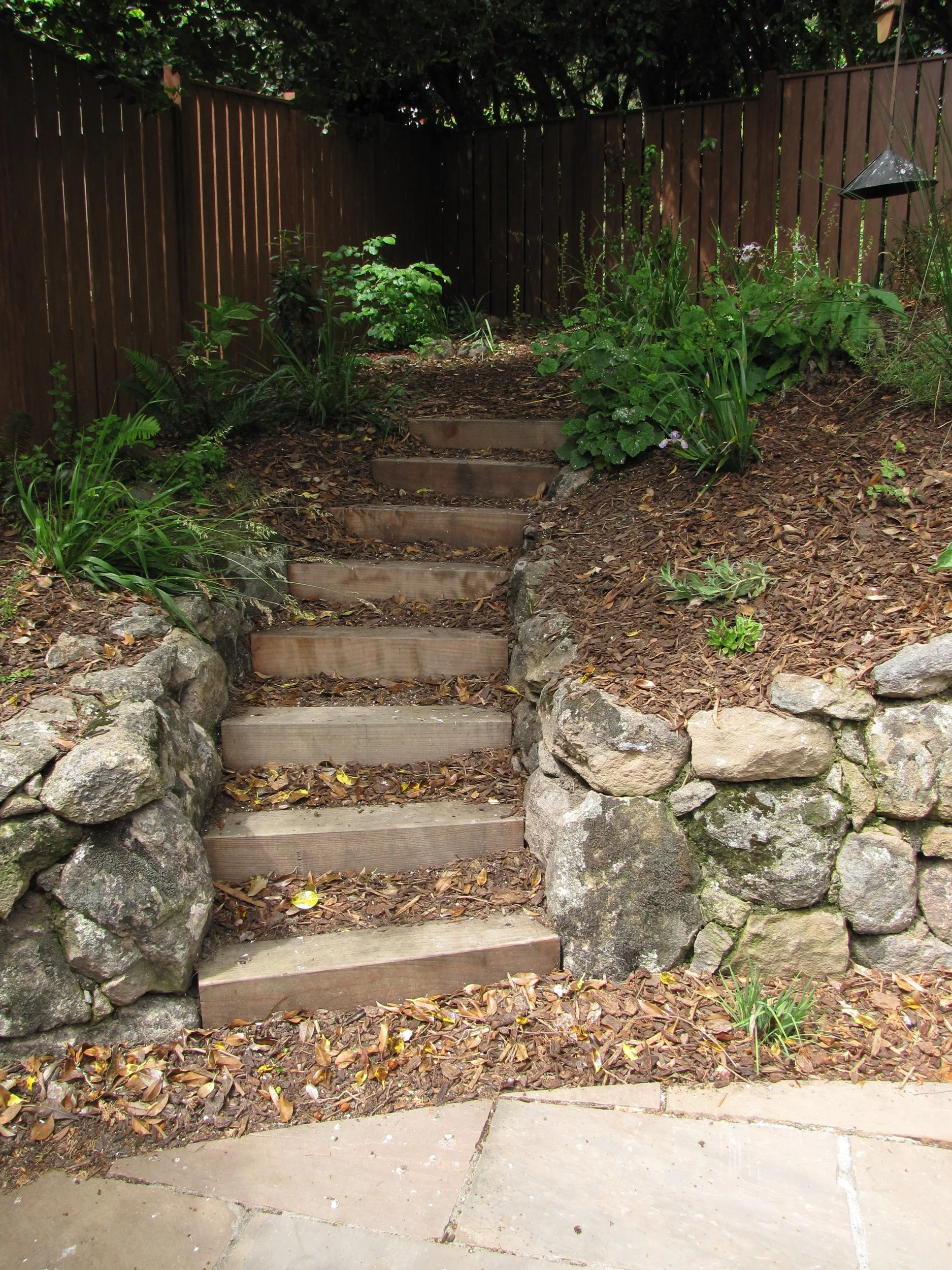 Timber tie steps up a berkeley hillside garden with moss rock retaining walls and a stone patio