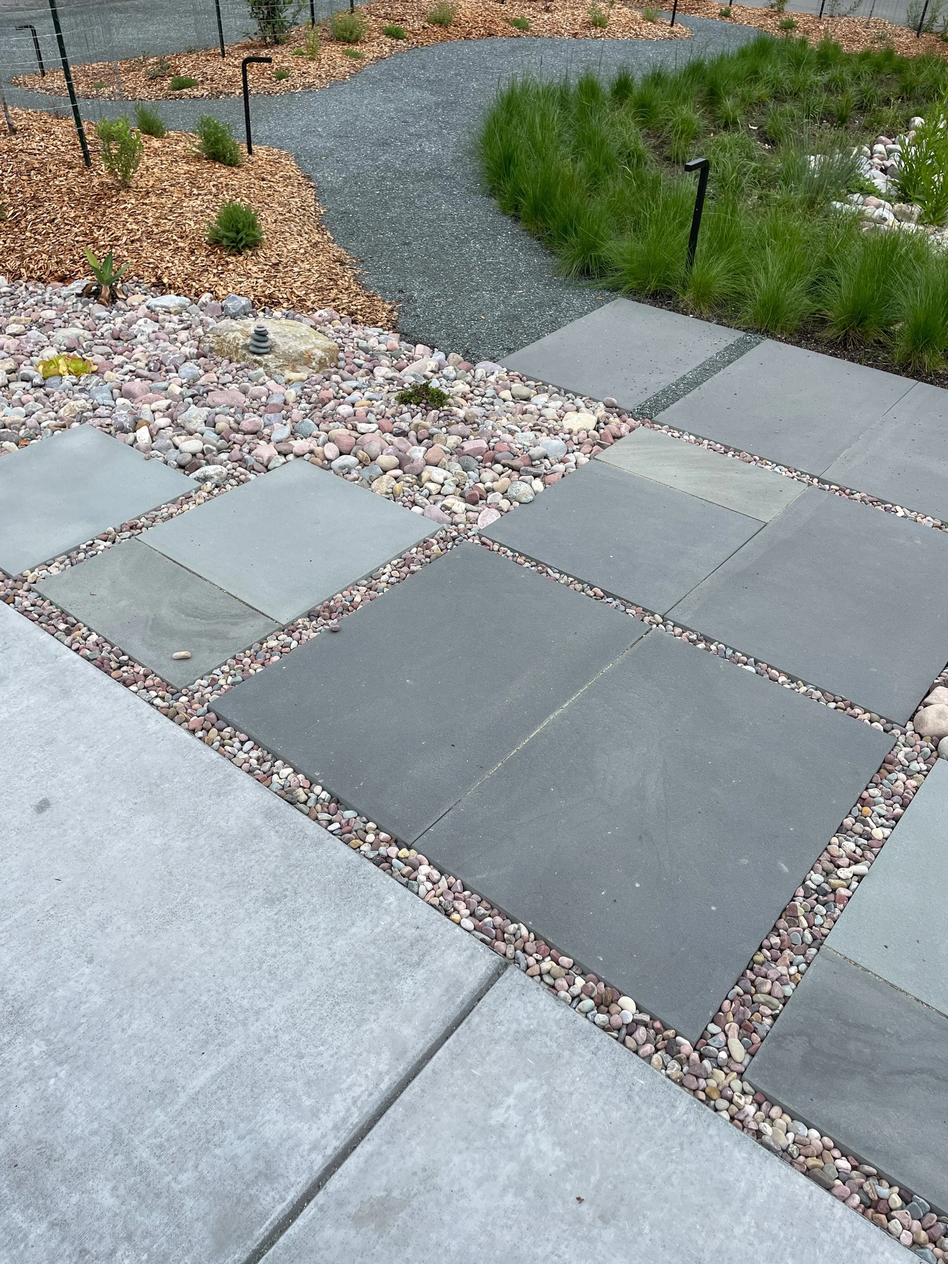 A bluestone pathway off of a concrete driveway with grey gravel and a california native meadow grassland.