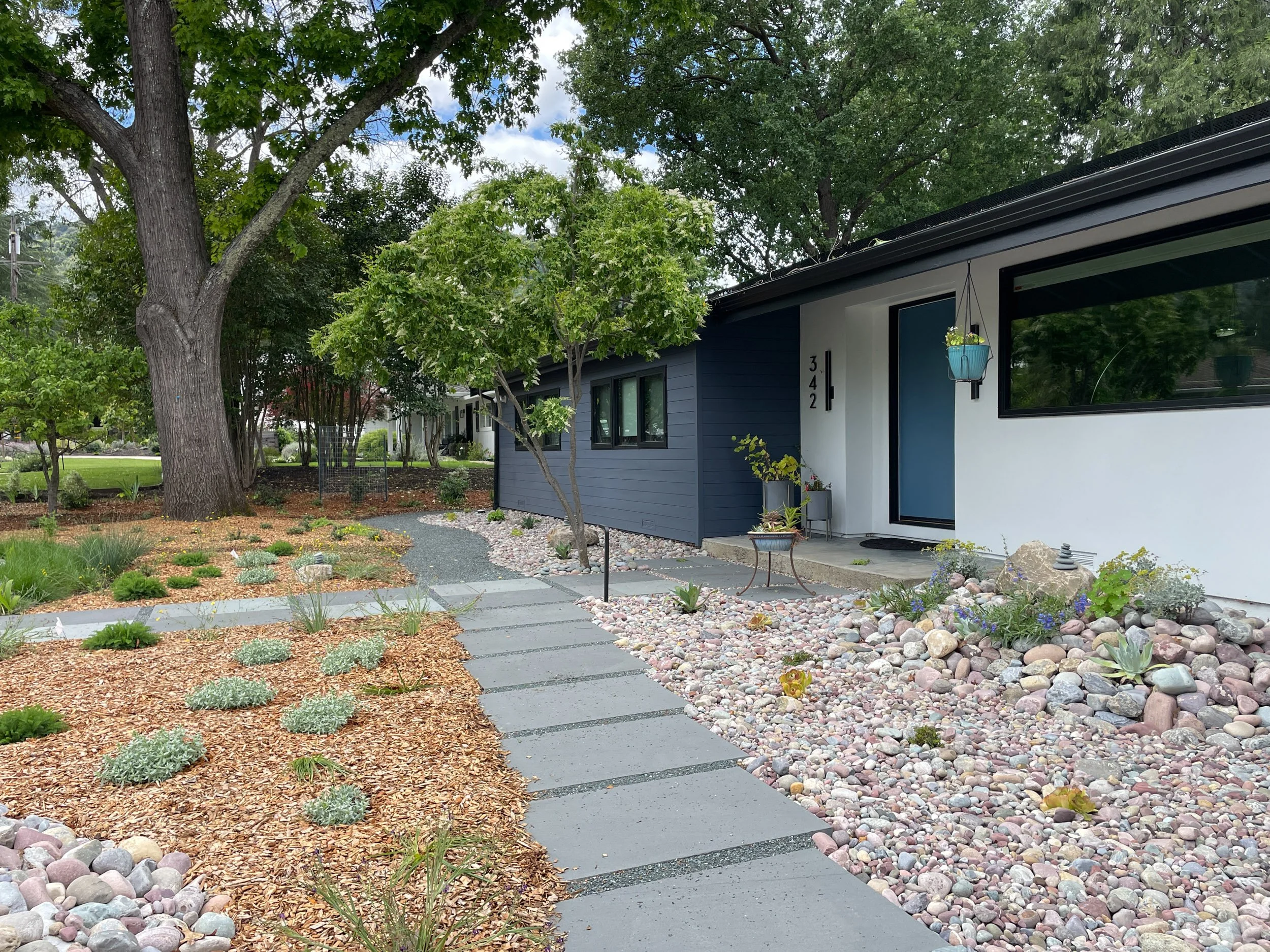 A 5 foot wide gravel mulch planting bed with low california native plants and a bluestone pathway helps to protect this residential home from wildfire.
