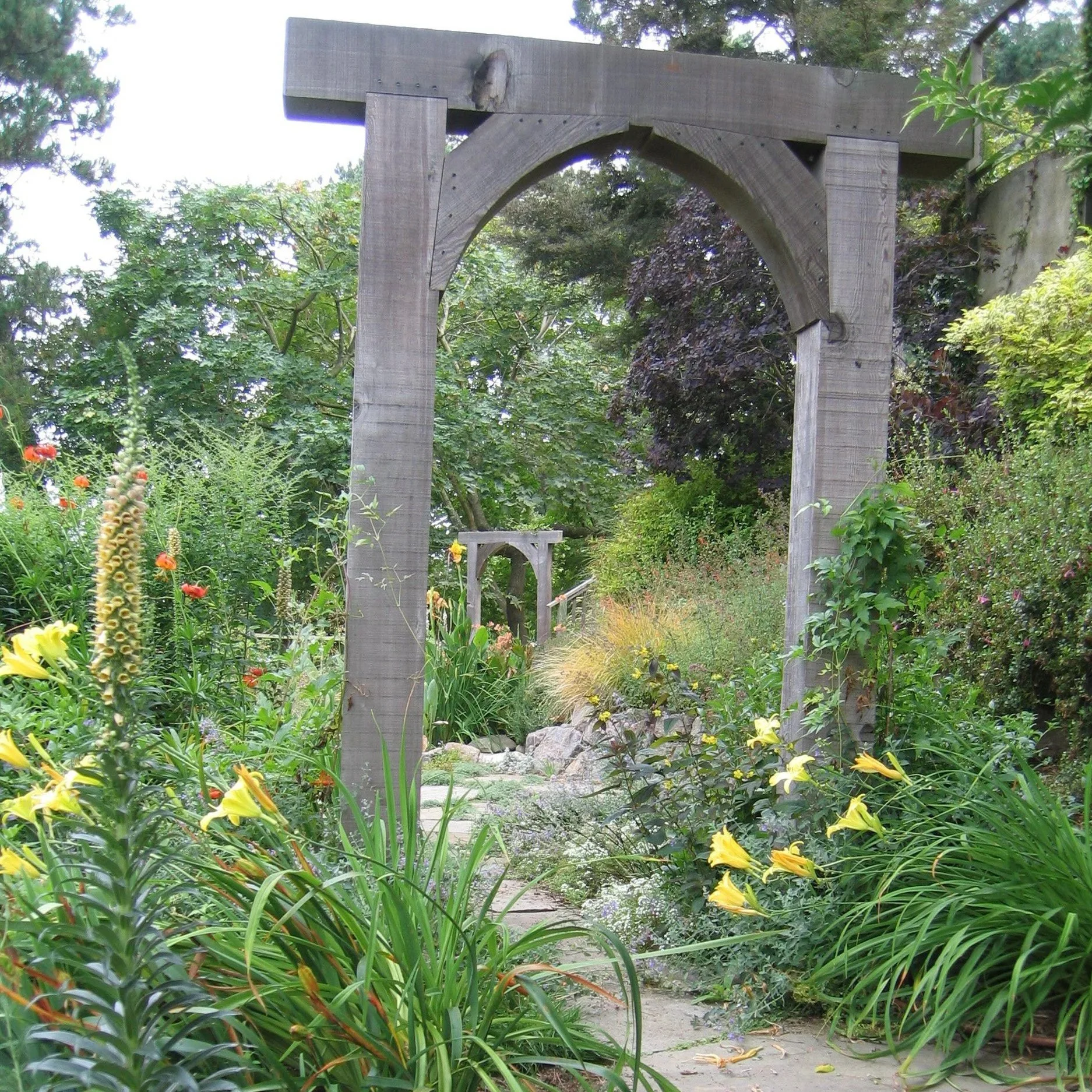A rounded wood arbor invites you to enter this hillside garden on a flagstone pathway with ground cover joints.