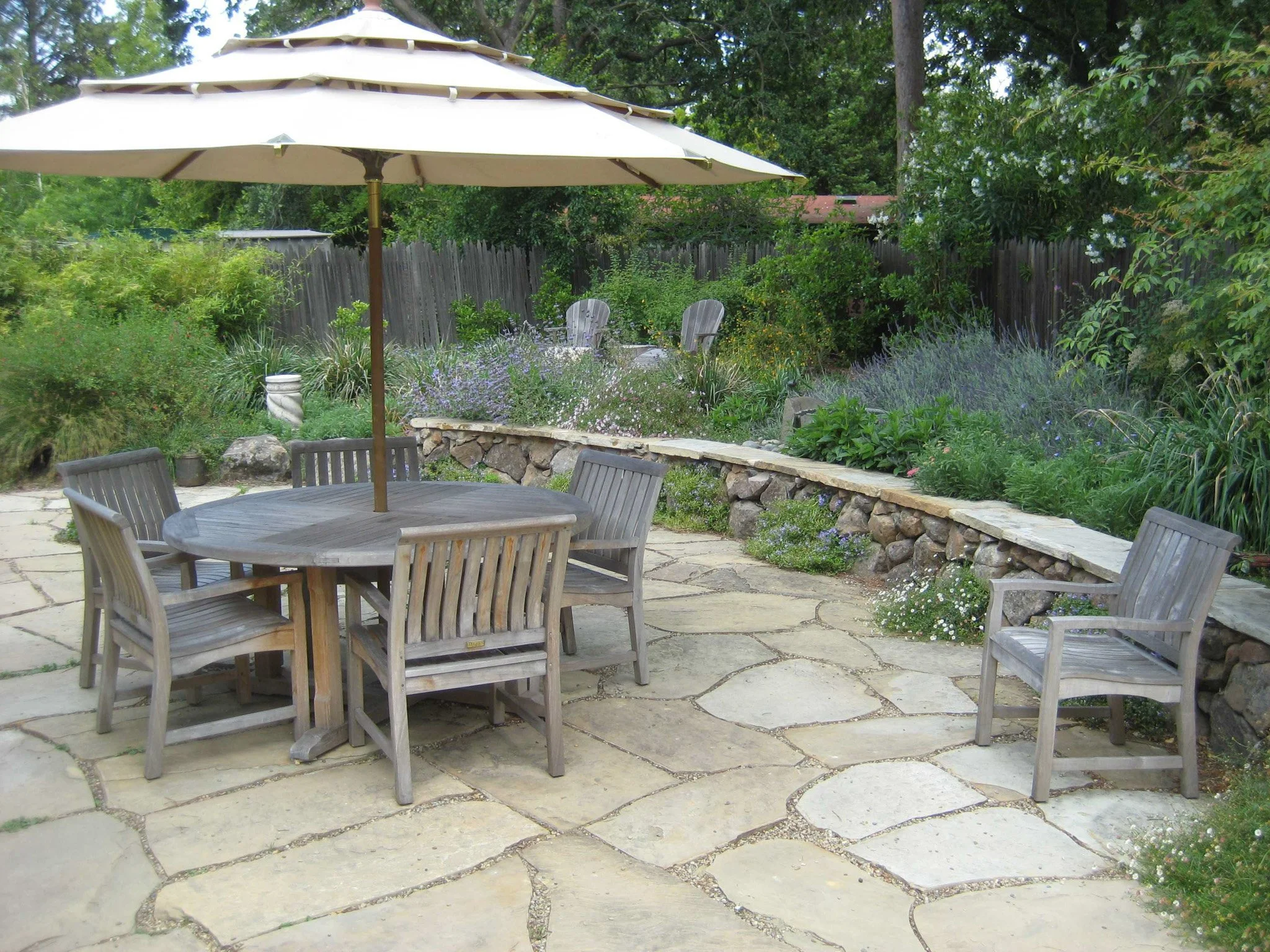 A natural flagstone patio with wood furniture and a low moss rock stone wall with a flat flagstone seat wall top surrounded by california native plants.