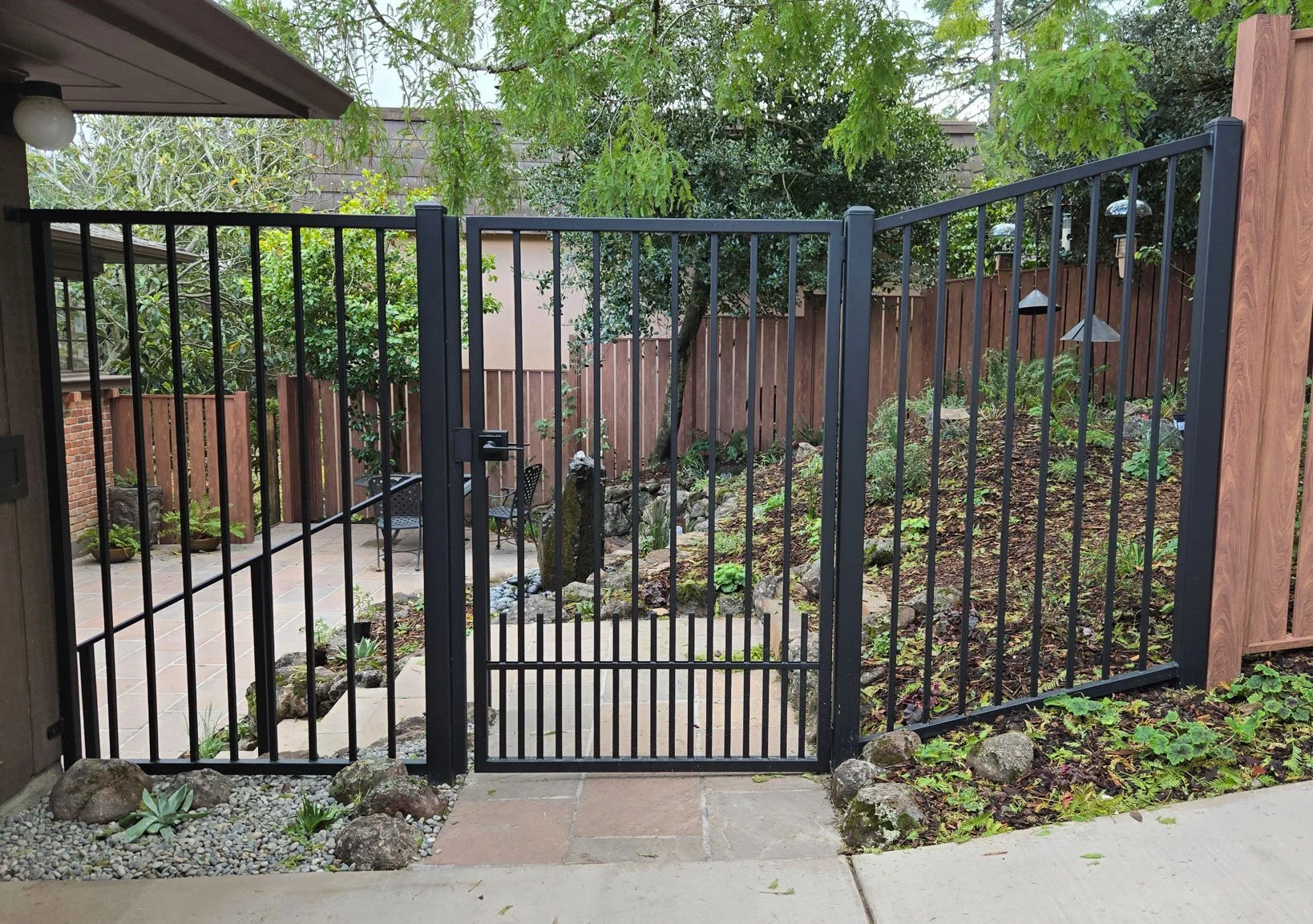 The front gate of this Berkeley hills garden is metal for fire safety while maintaining a welcoming open view to the california native plant bird-friendly garden and fountain next to a stone patio