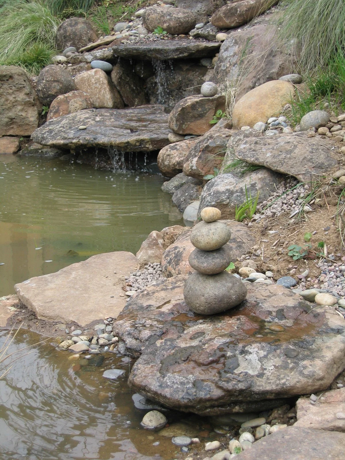 Natural waterfall stone pond water feature with stacked stone cairn.