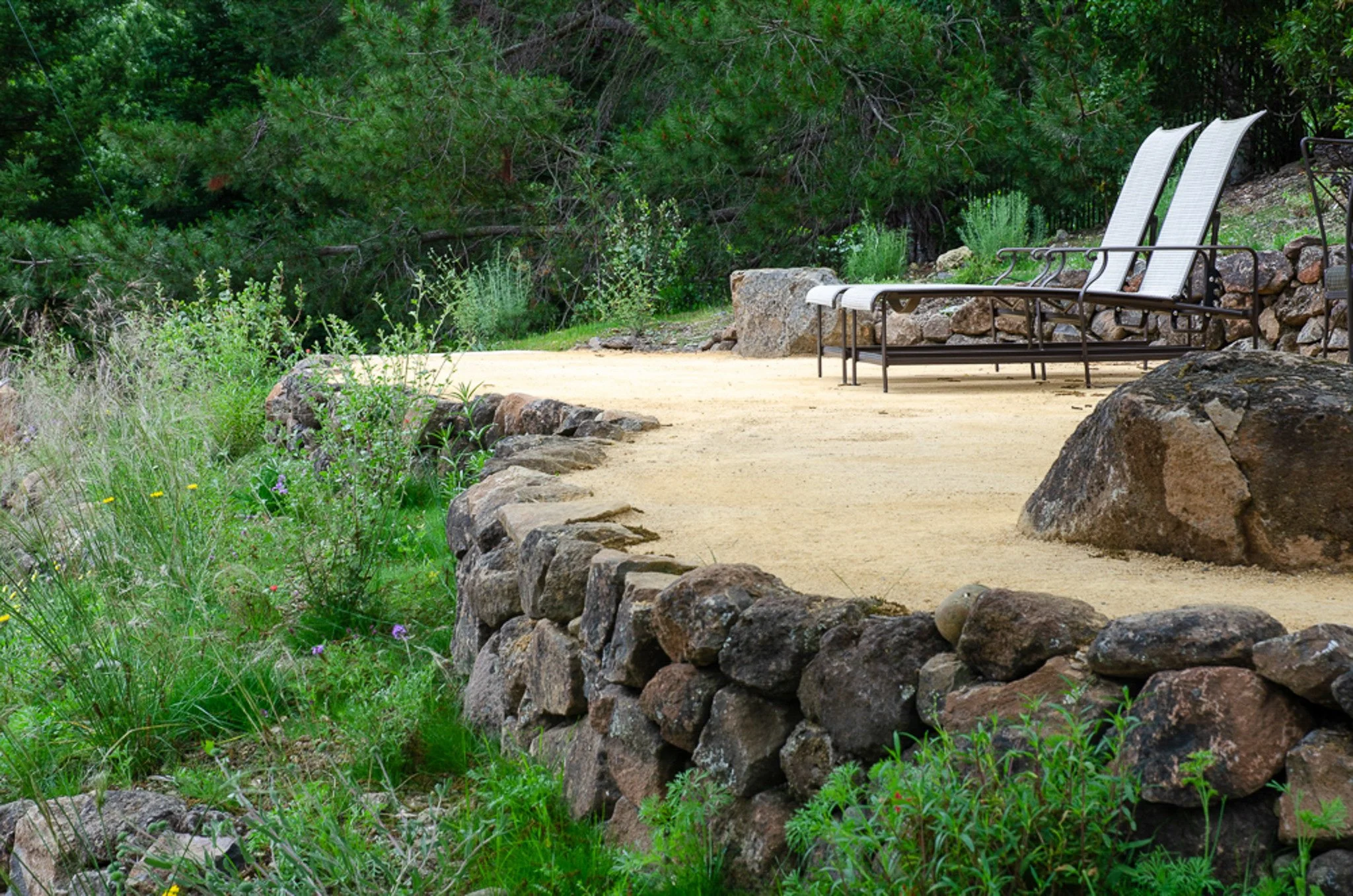 Dry stacked moss rock stone wall with california native plants in front of a tan decomposed granite patio.