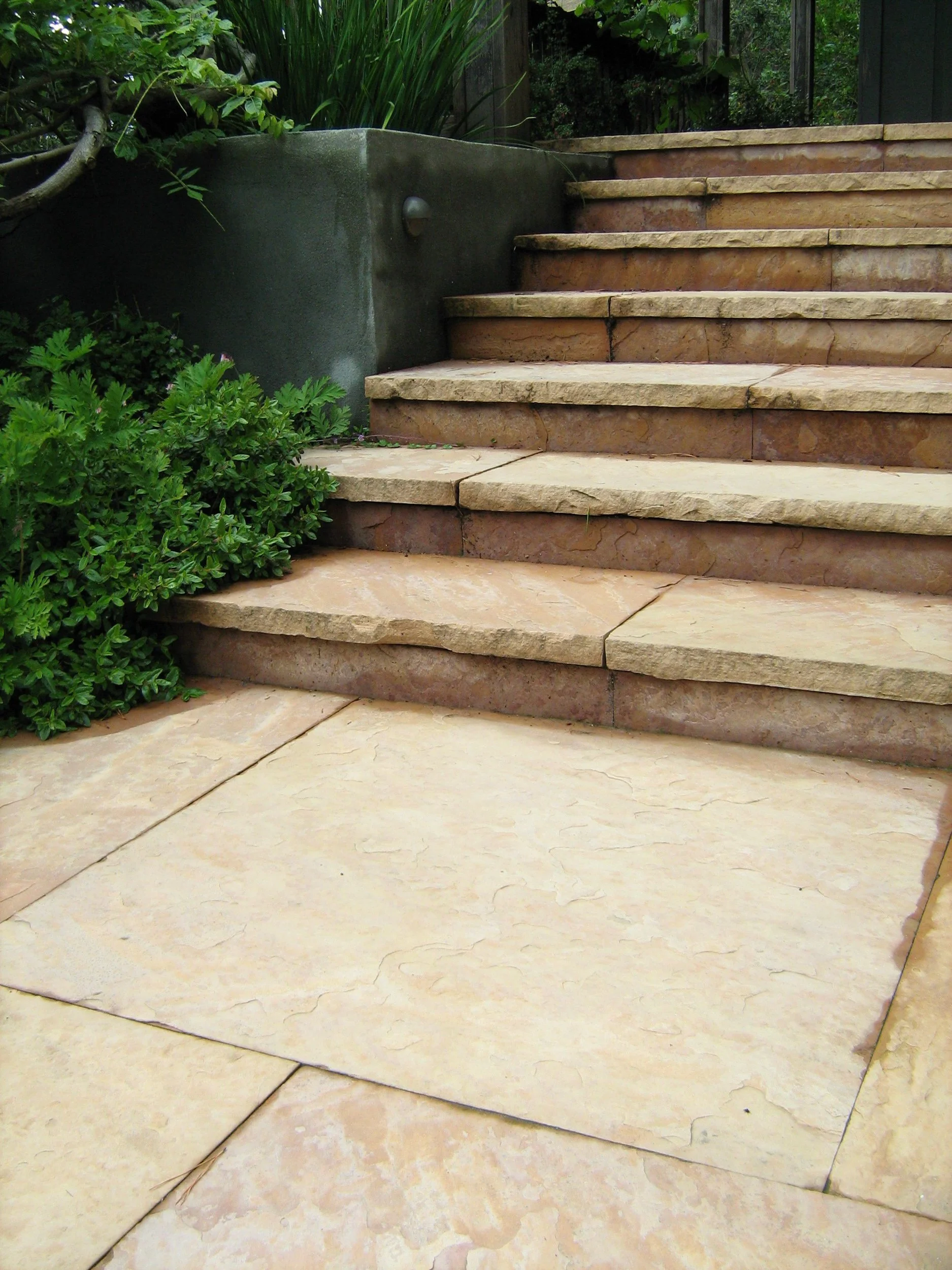 A formal stone geometric tan patio with steps into a residential garden.