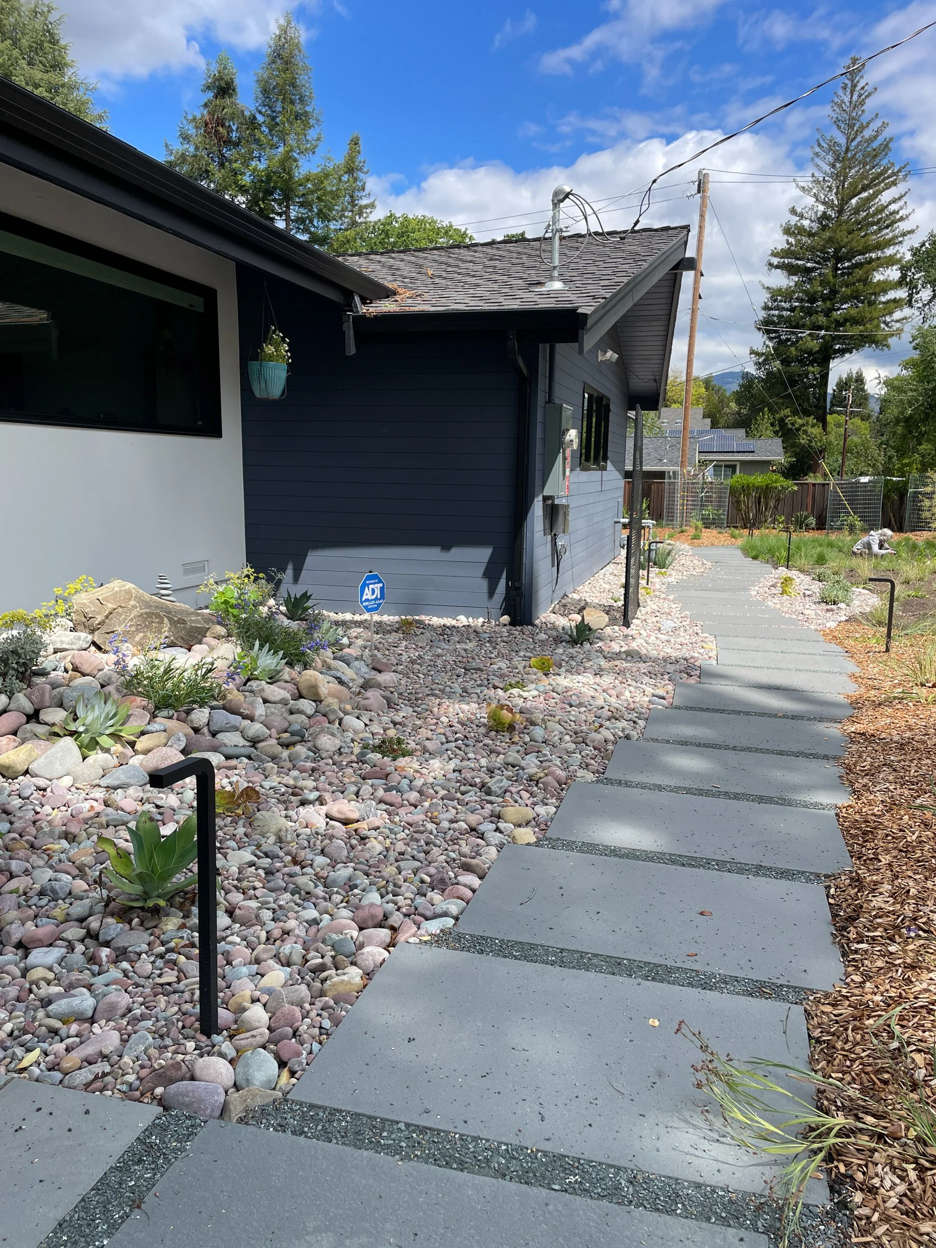 A 5 foot wide gravel mulch planting bed with low california native plants and a bluestone pathway helps to protect this residential home from wildfire.