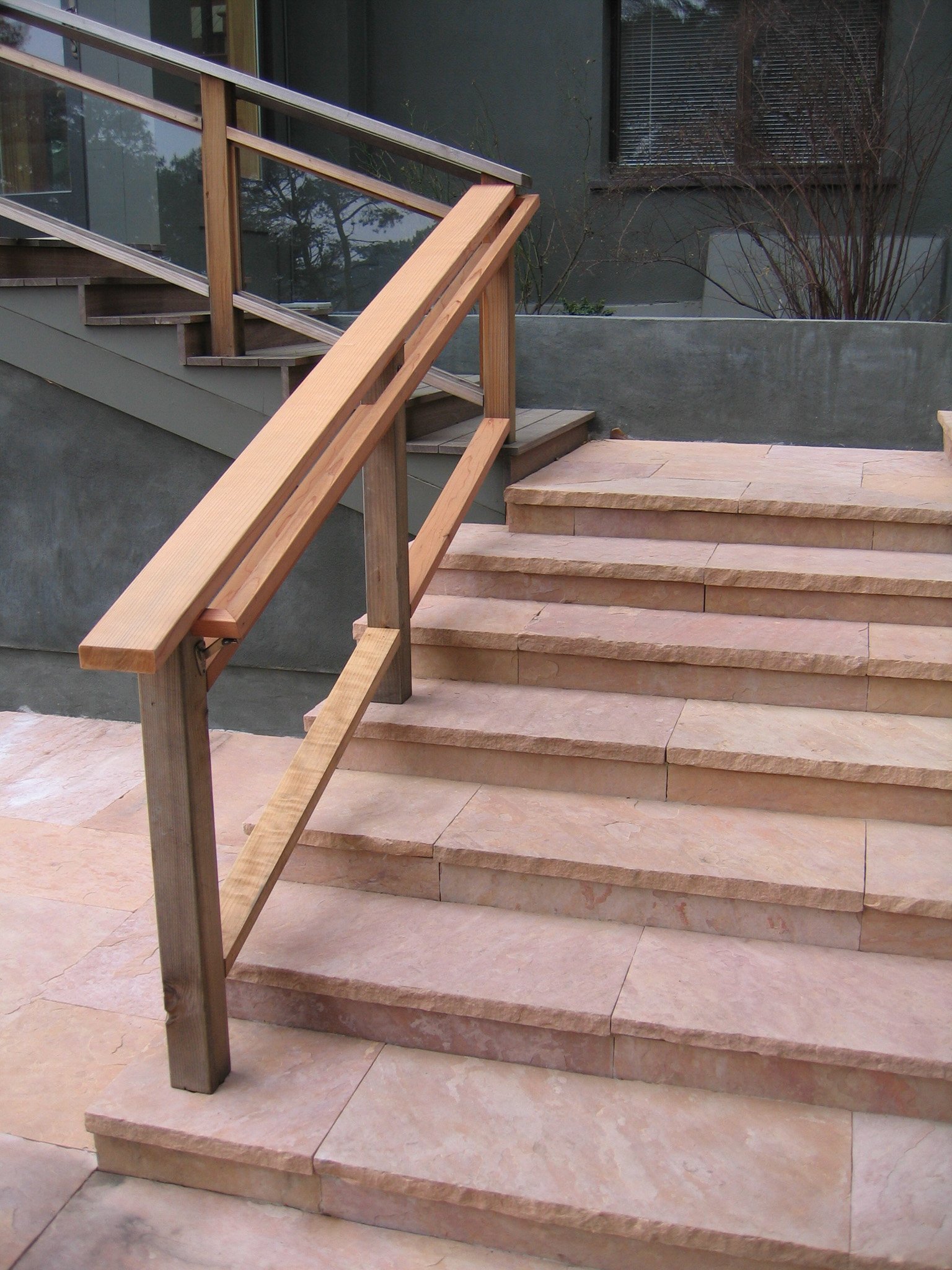 Wood railing down pink stone landscape steps next to grey concrete walls