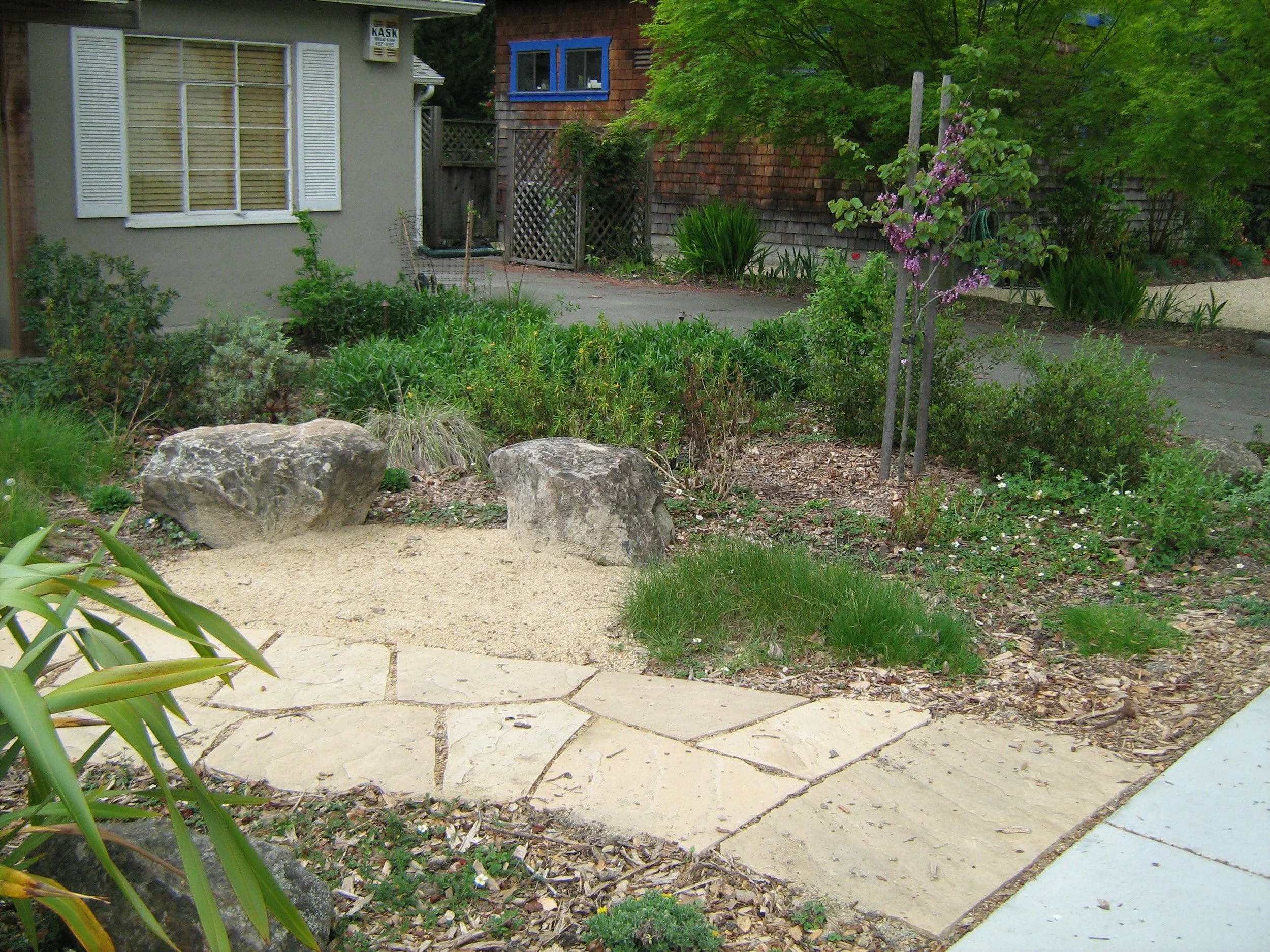 A tan natural flagstone pathway next to a decomposed granite patio with boulder seating in a california native front residential garden.