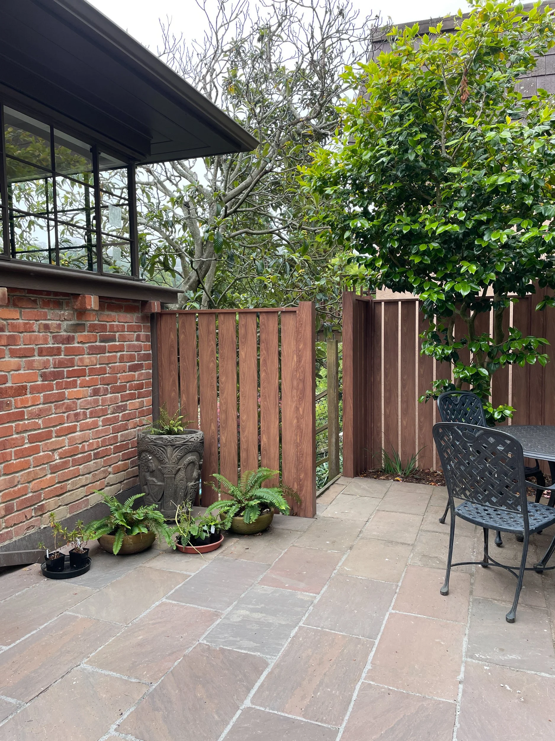 Stone steps and patio with potted plants next to a metal fence and gate in a berkeley hills firesafe residential garden