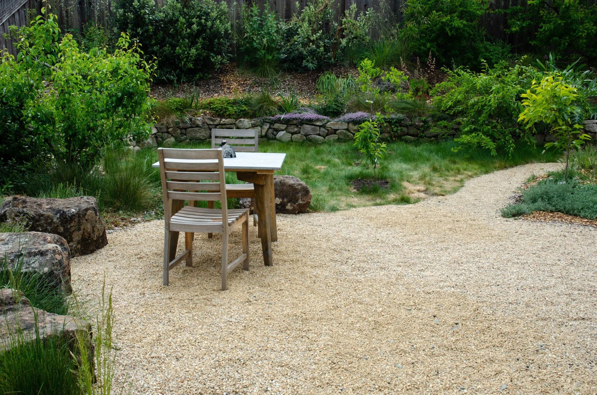 A tan gravel patio with seating and boulders in a california native plant residential garden.