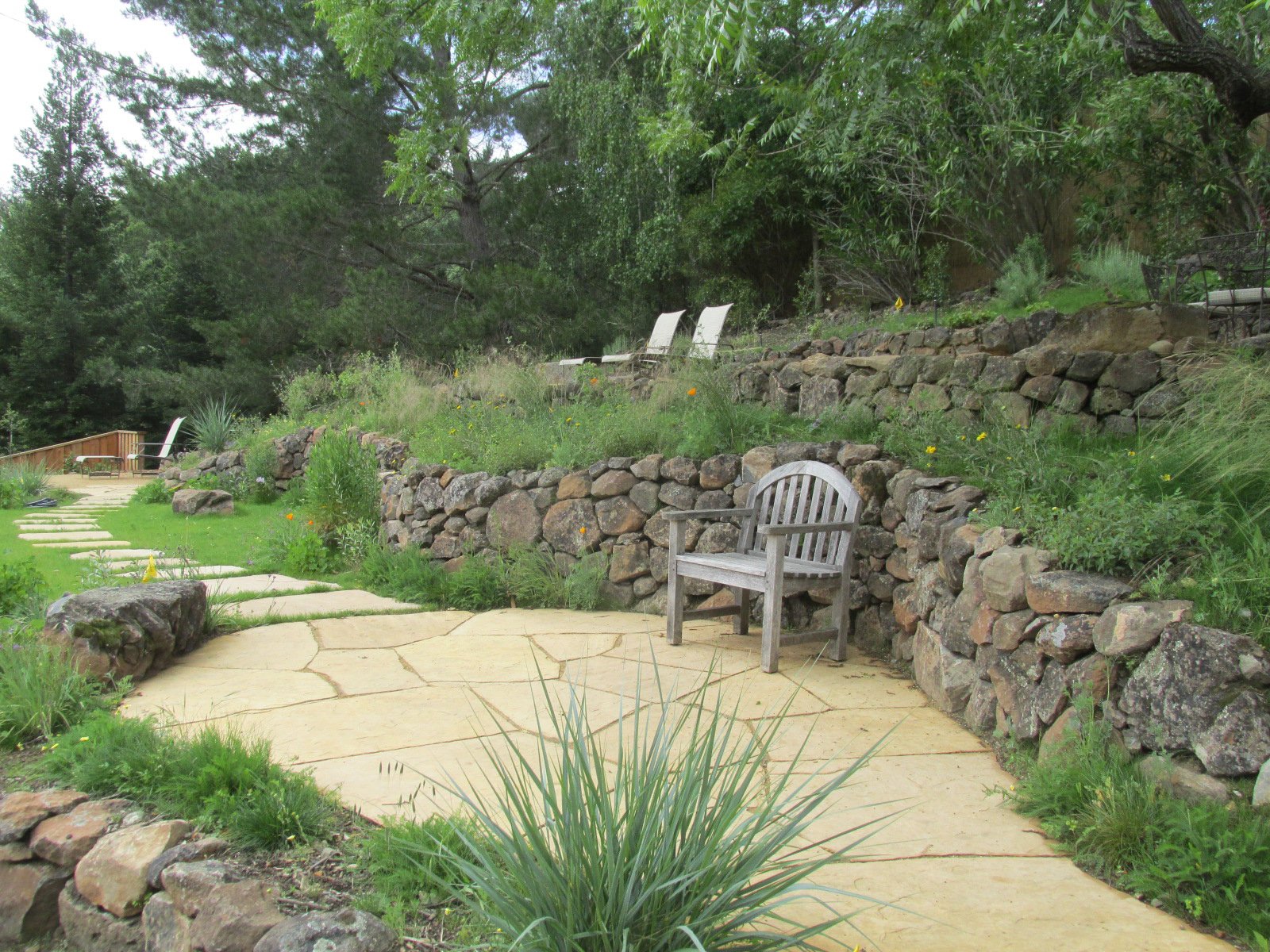 A wood bench tucked into an alcove of the natural stone wall on a flagstone patio, looking out over this hillside wildlife garden.