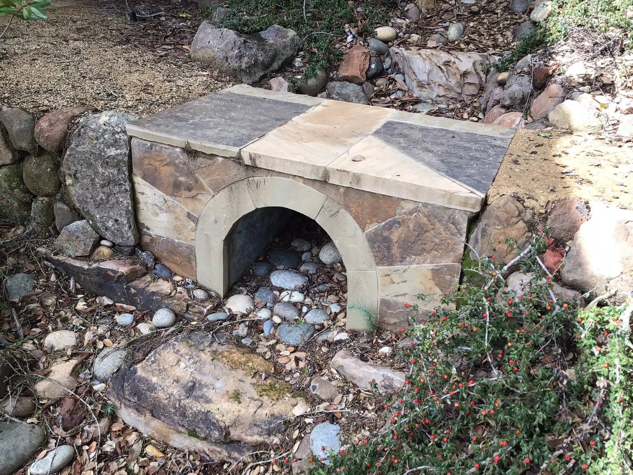 A low stone bridge connects a decomposed granite pathway over a seasonal creek.
