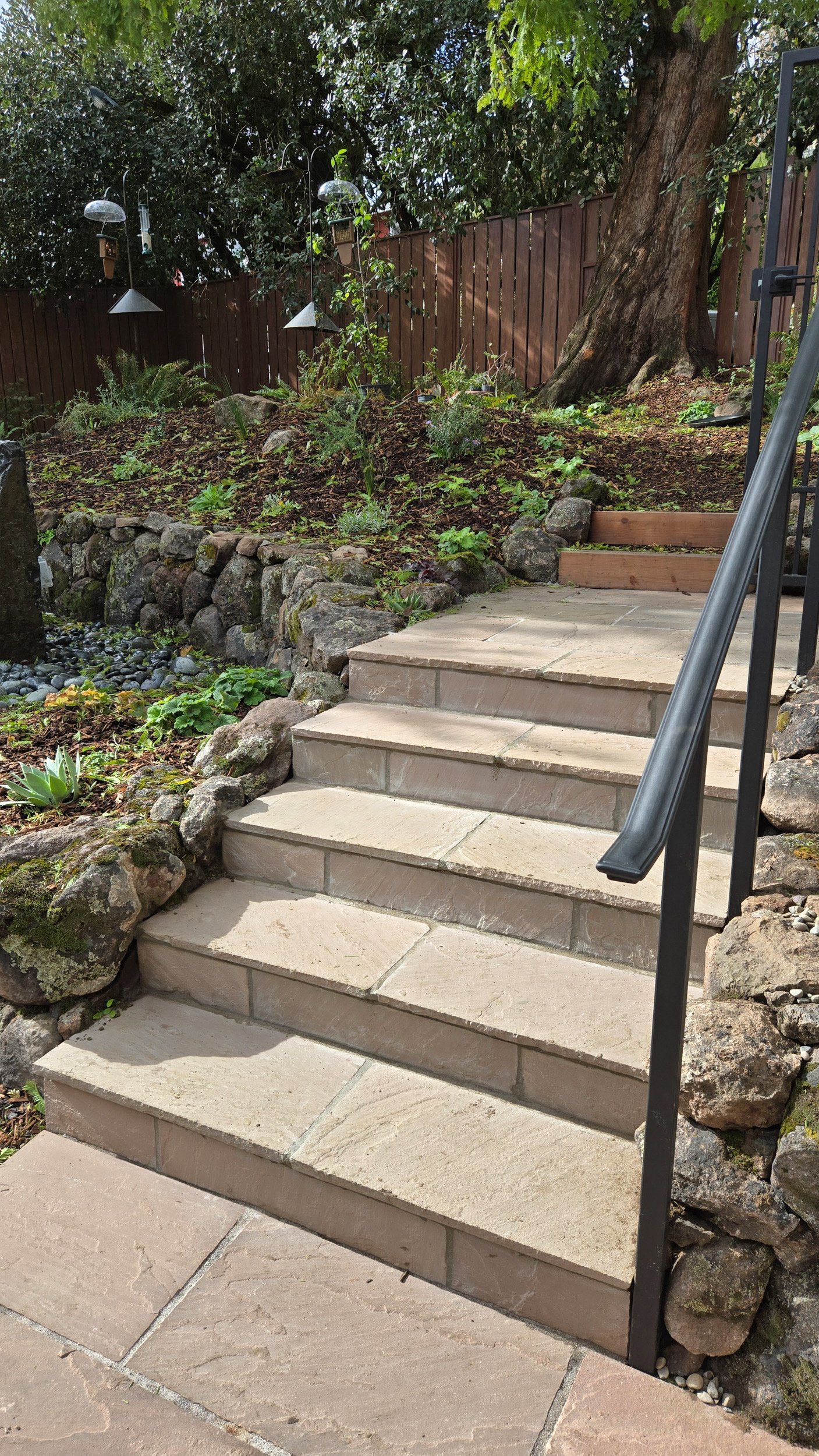 Formal stone paver steps with a metal railing with moss rock dry stacked stone walls in a california native plant residential garden.