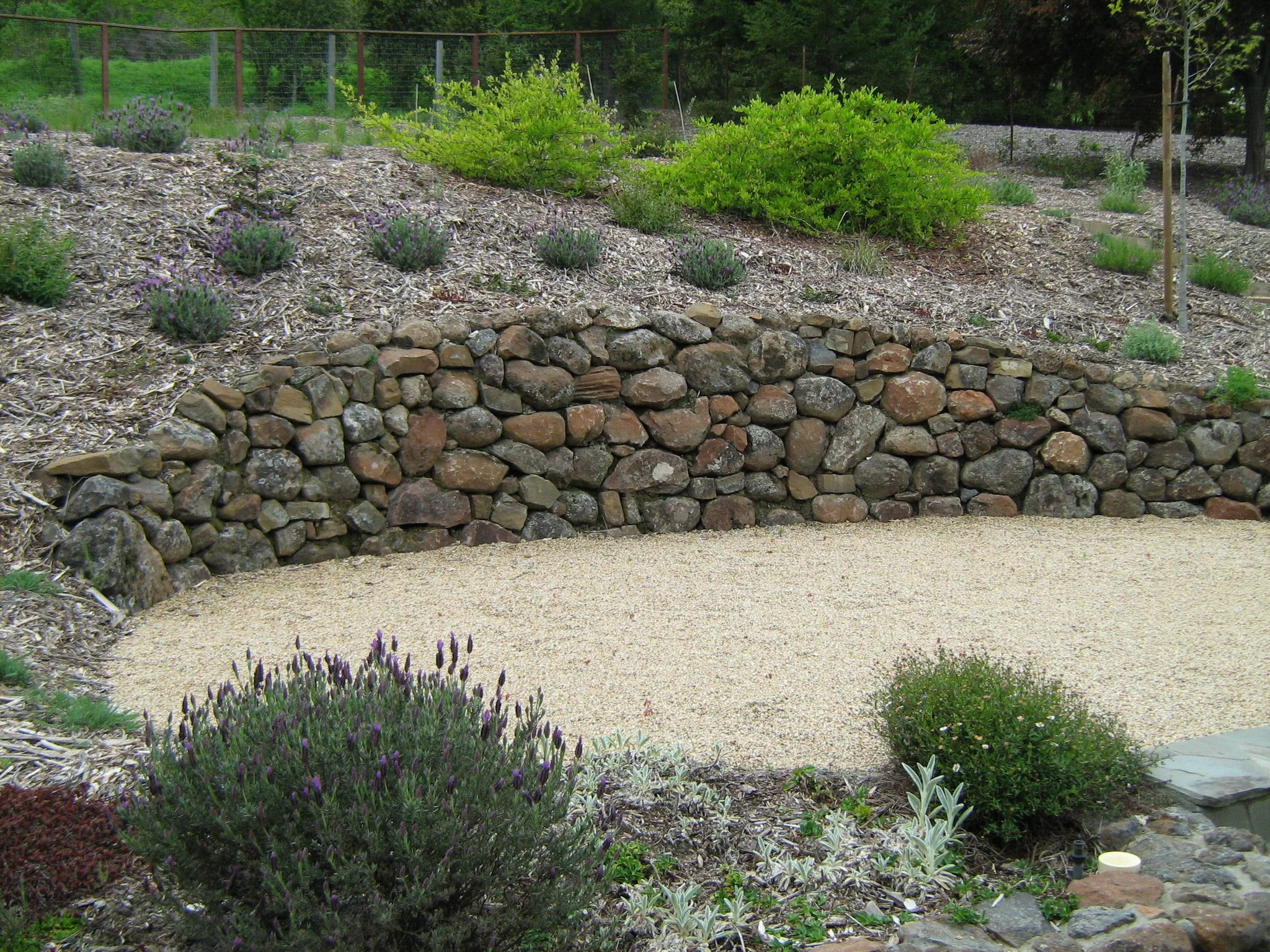 Curved dry stacked round stone wall in front of tan gravel patio.