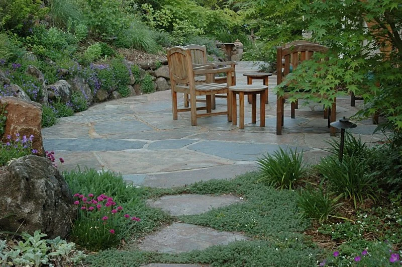 A natural flagstone patio with wood furniture and a low moss rock stone wall.