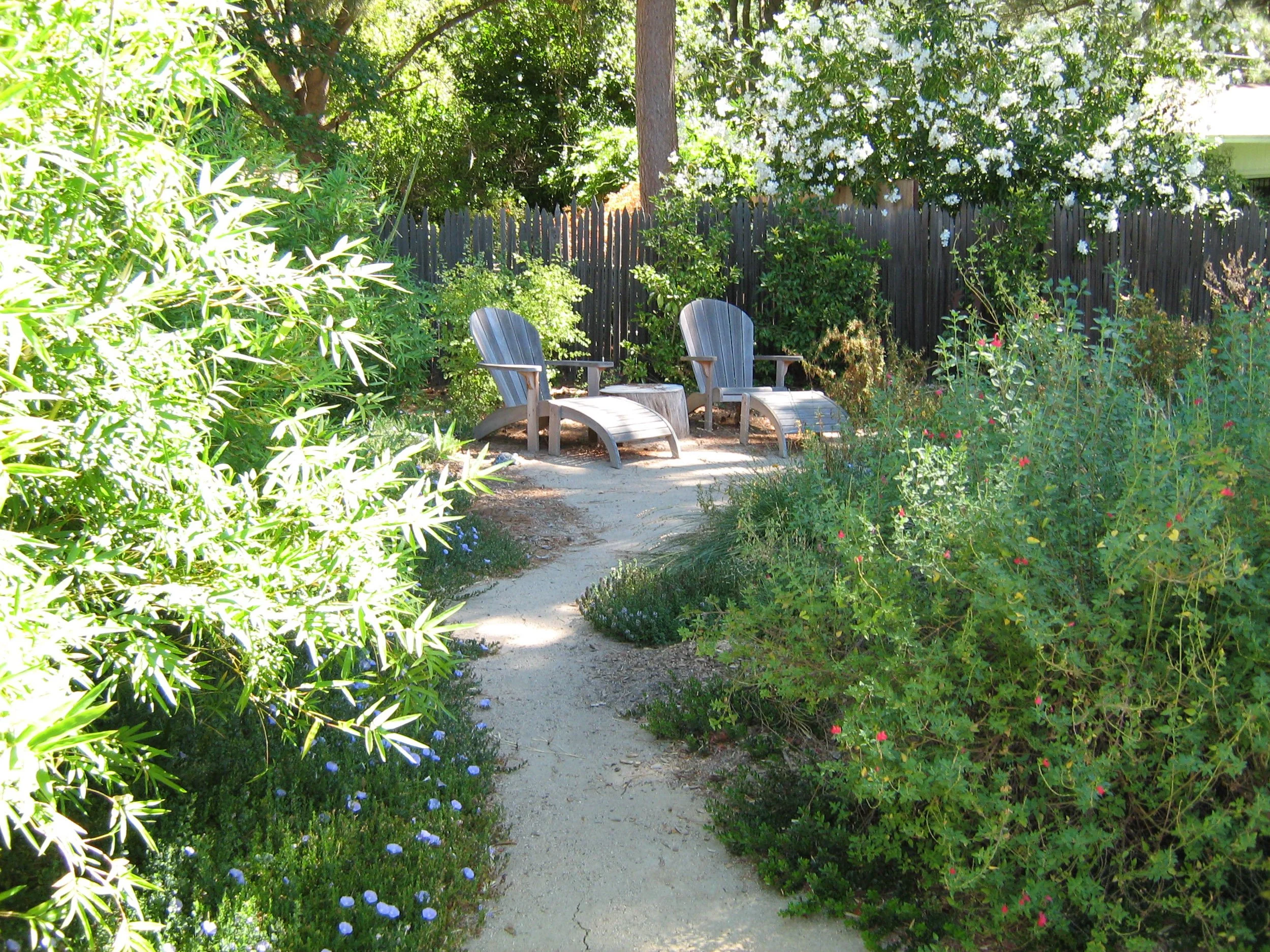 A decomposed granite pathway leads to a patio with natural wood adirondack lounge chairs surrounded by california native plants.