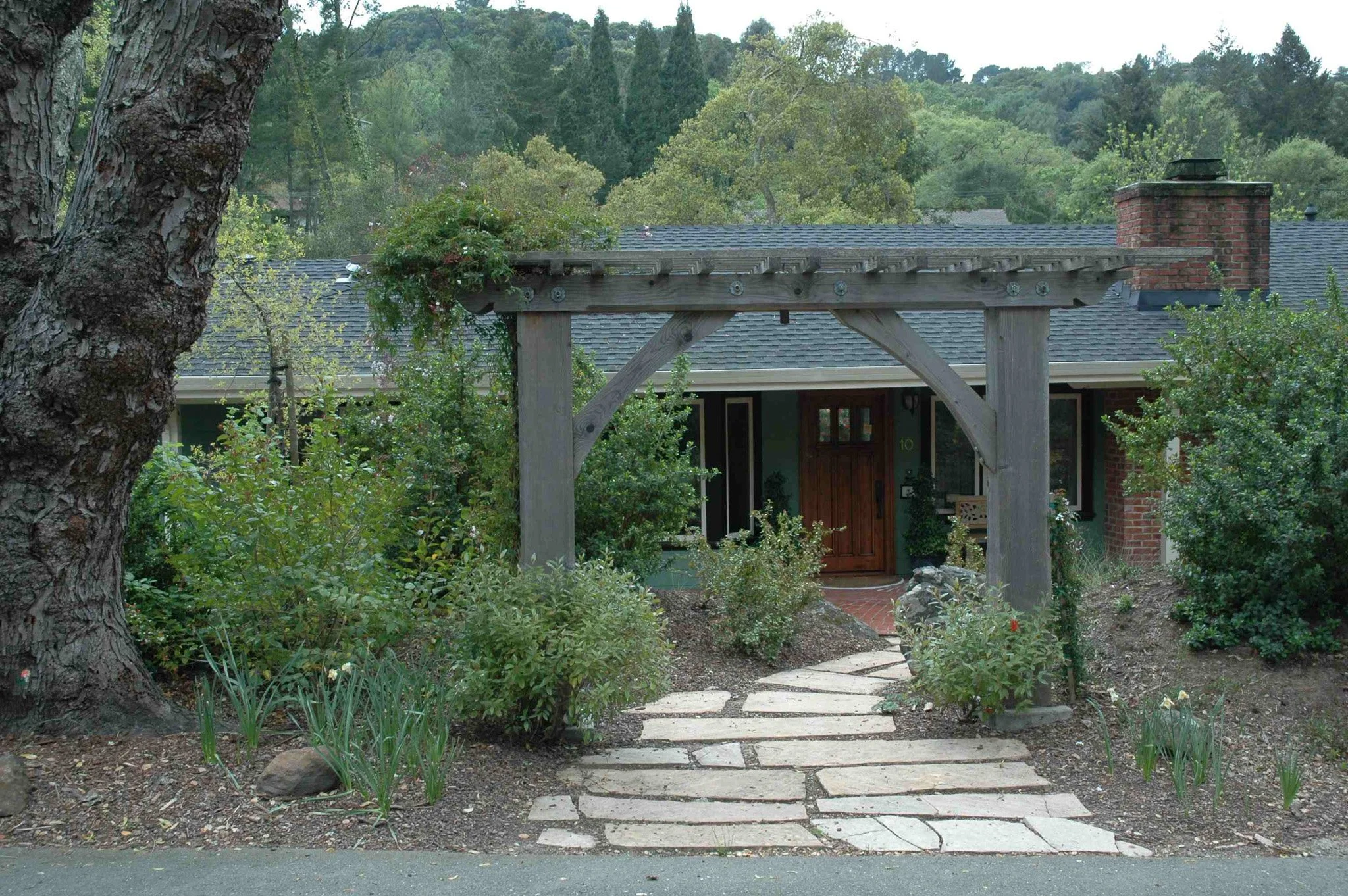 A wood pergola arbor overhead garden structure entrance to a residential home with california native plants