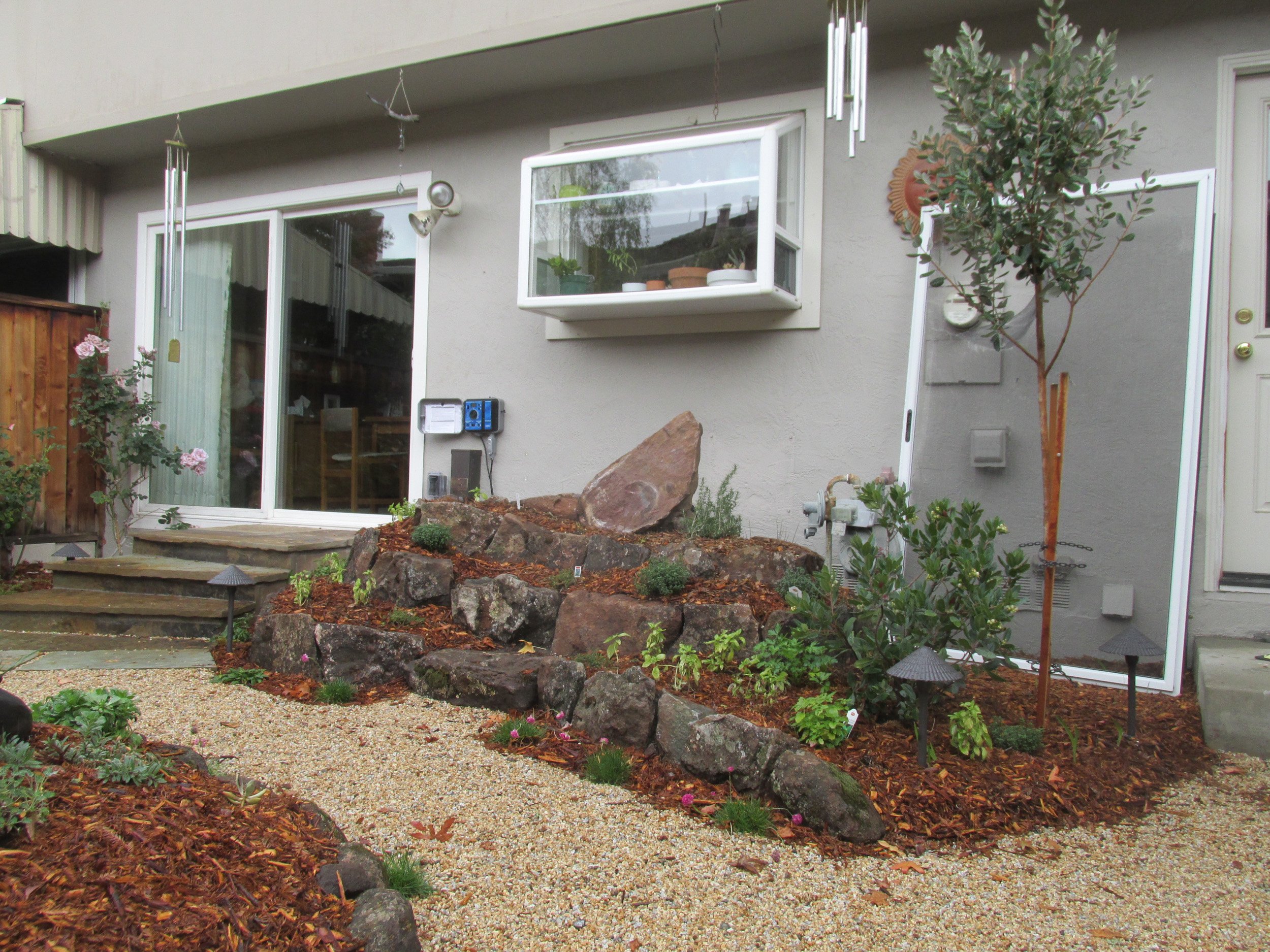 Stones and boulders form a raised spiral herb garden in a residential landscape.