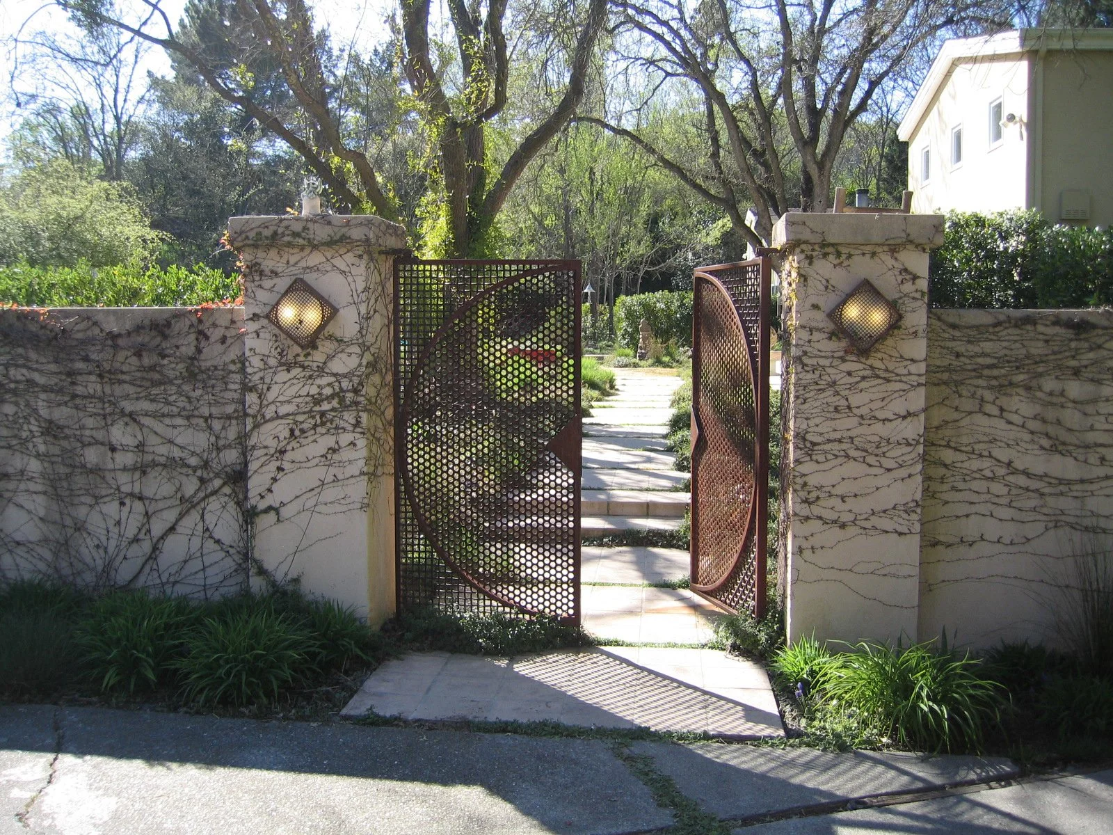 A corten steel round garden entry gate with round gold landscape lights on stucco columns