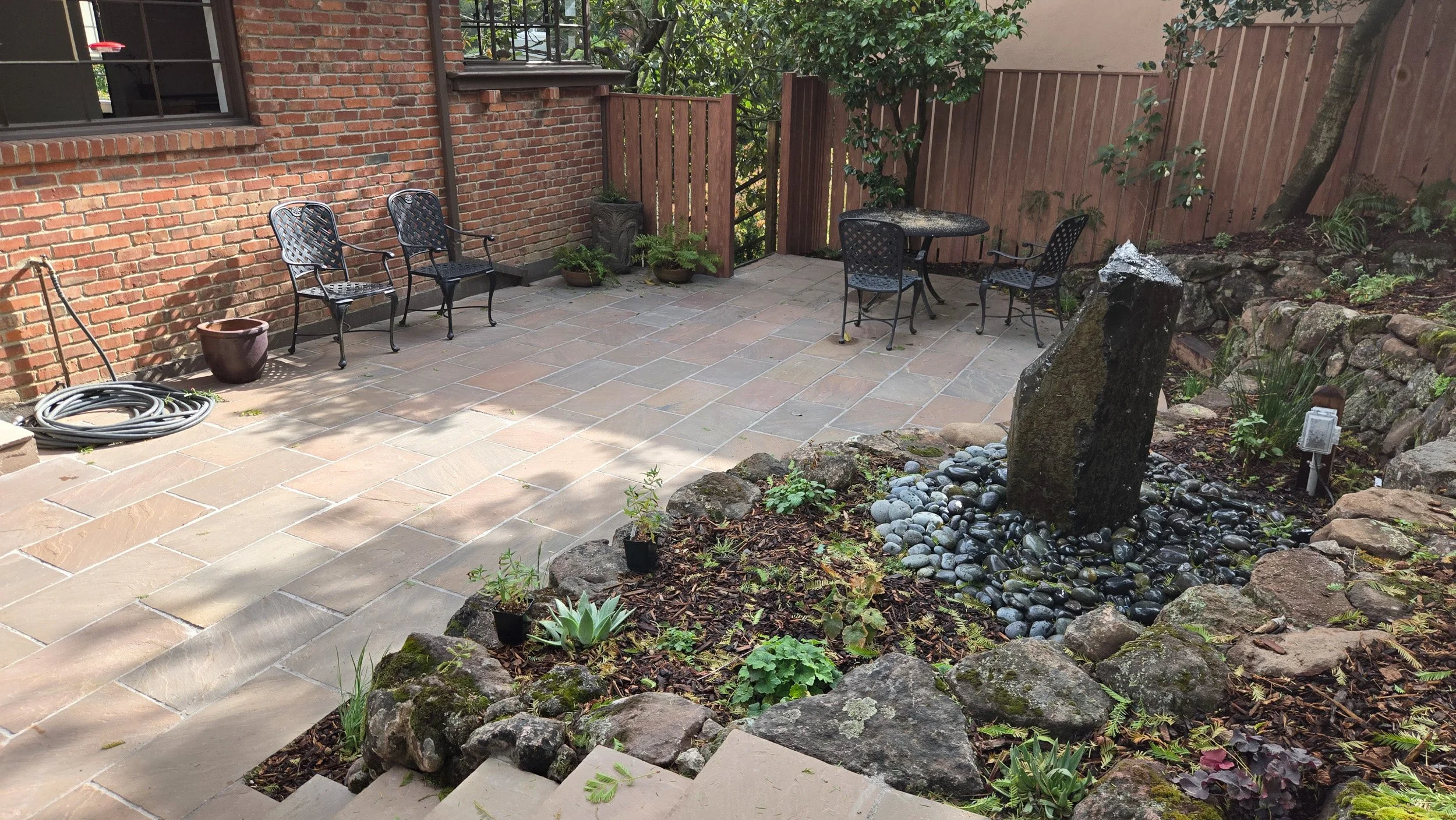 A geometric stone patio and an aluminum fence with a wood look helps to protect this california native plant garden from fire.