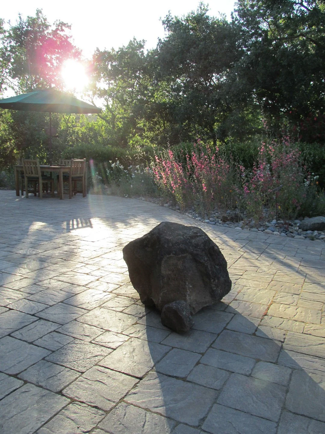 A boulder sits in the center of a geometric stone patio.