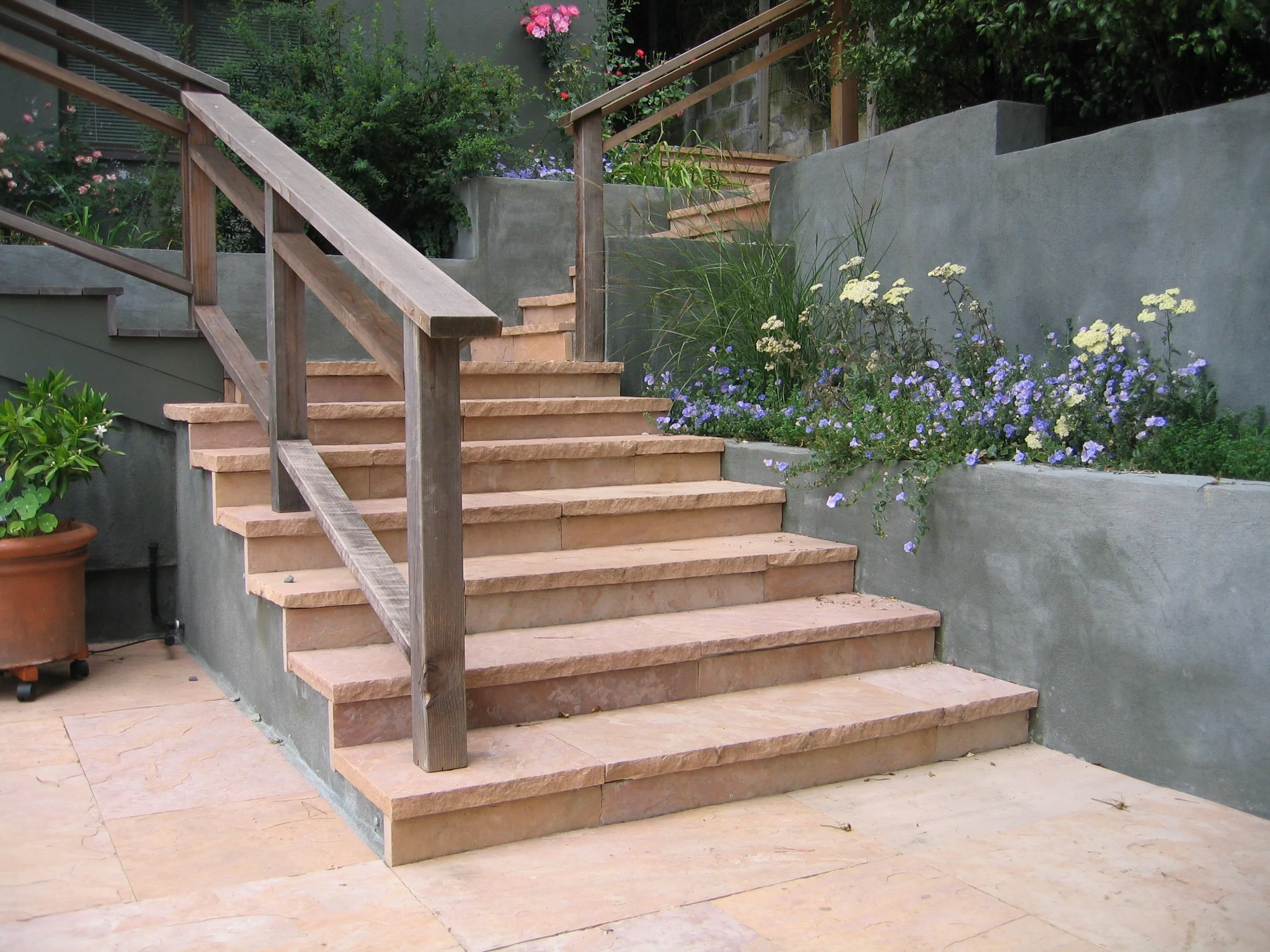 Flagstone steps with a wood railing descend onto a modern geometric stone patio.