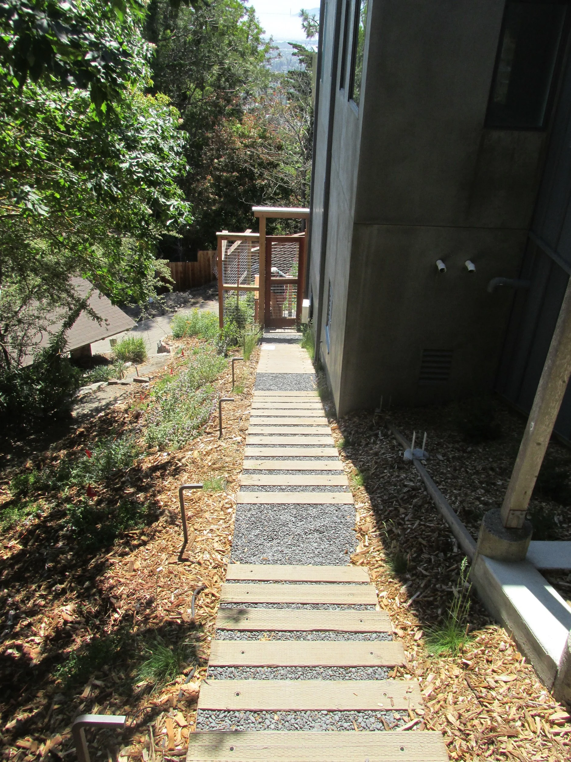 Timber tie steps with grey gravel backfill up a hillside on the side of a residence in a california native plant garden.